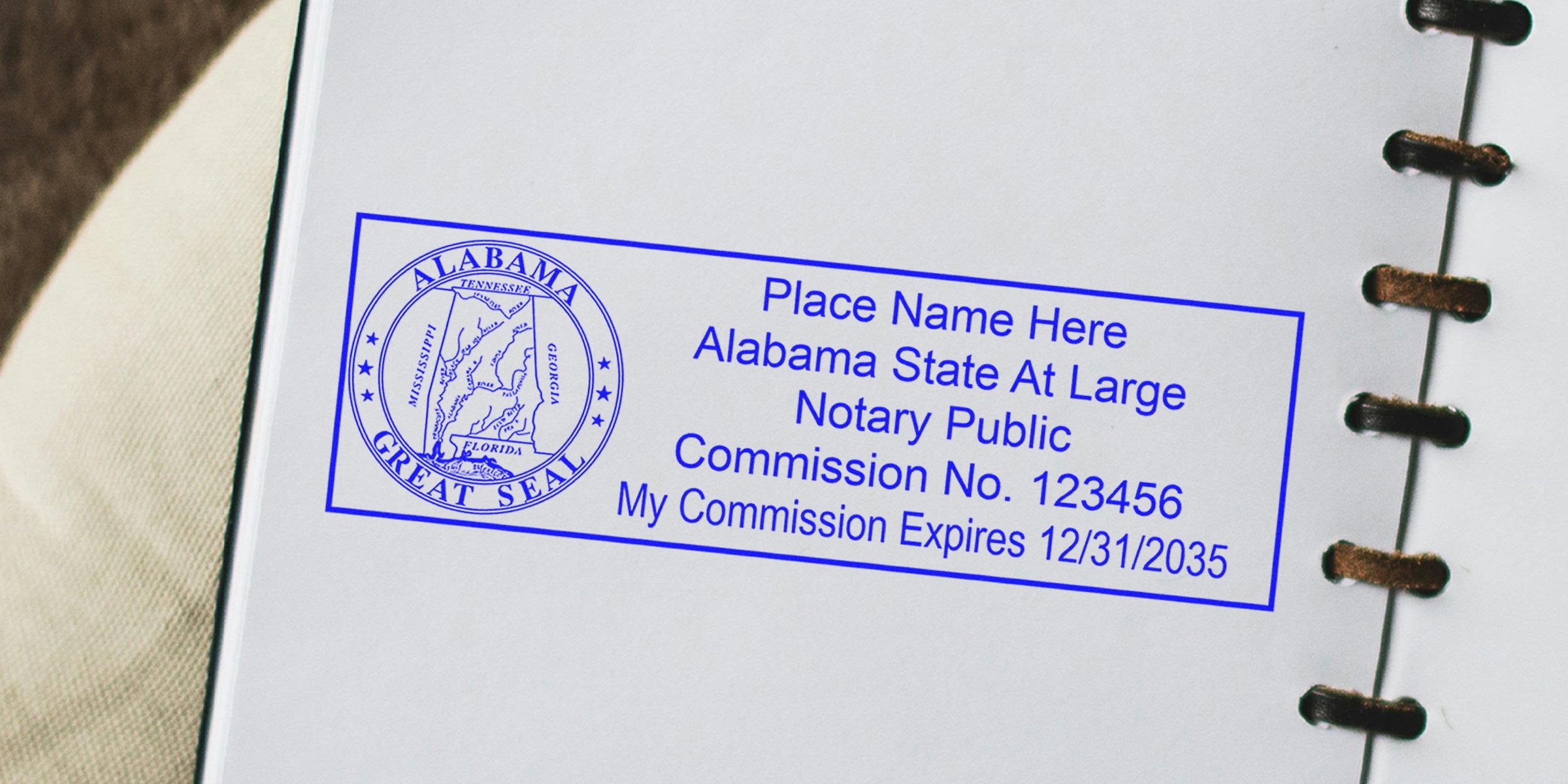 Blue Alabama notary public stamp on notebook page showing state great seal, placeholder name, commission number and expiration date, rectangular blue ink notary seal for official document authentication
