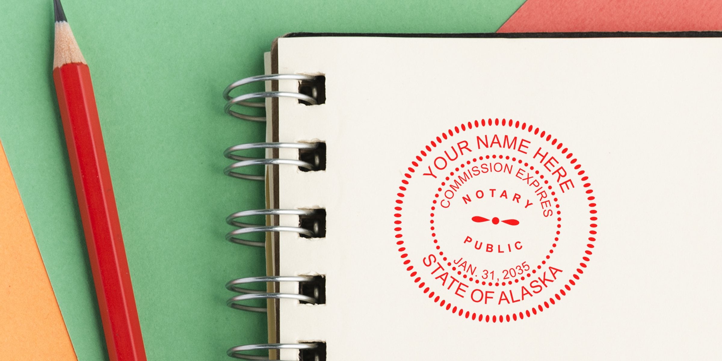 Close-up of spiral notebook page with red circular notary stamp reading "State of Alaska" and commission expiry Jan. 31, 2035, red pencil on green and orange paper background — office stationery, legal notary seal, document authentication image