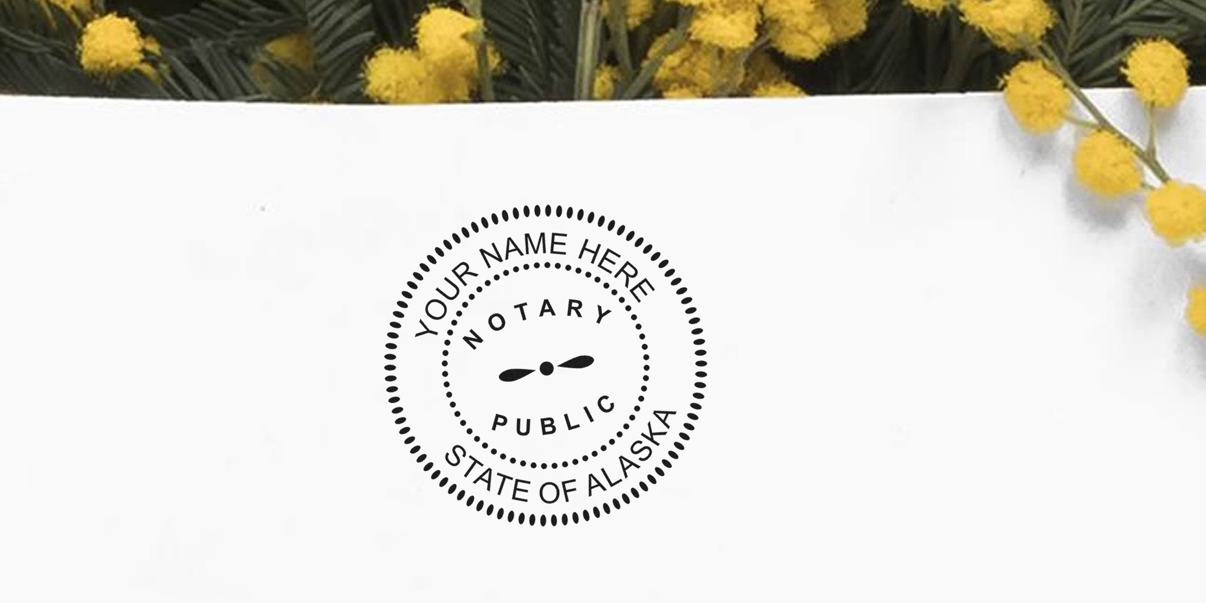 Round black "Notary Public - State of Alaska" stamp mockup reading "Your Name Here" on white paper with dotted border, centered below yellow mimosa flowers — notary seal mockup for Alaska notary services and branding.