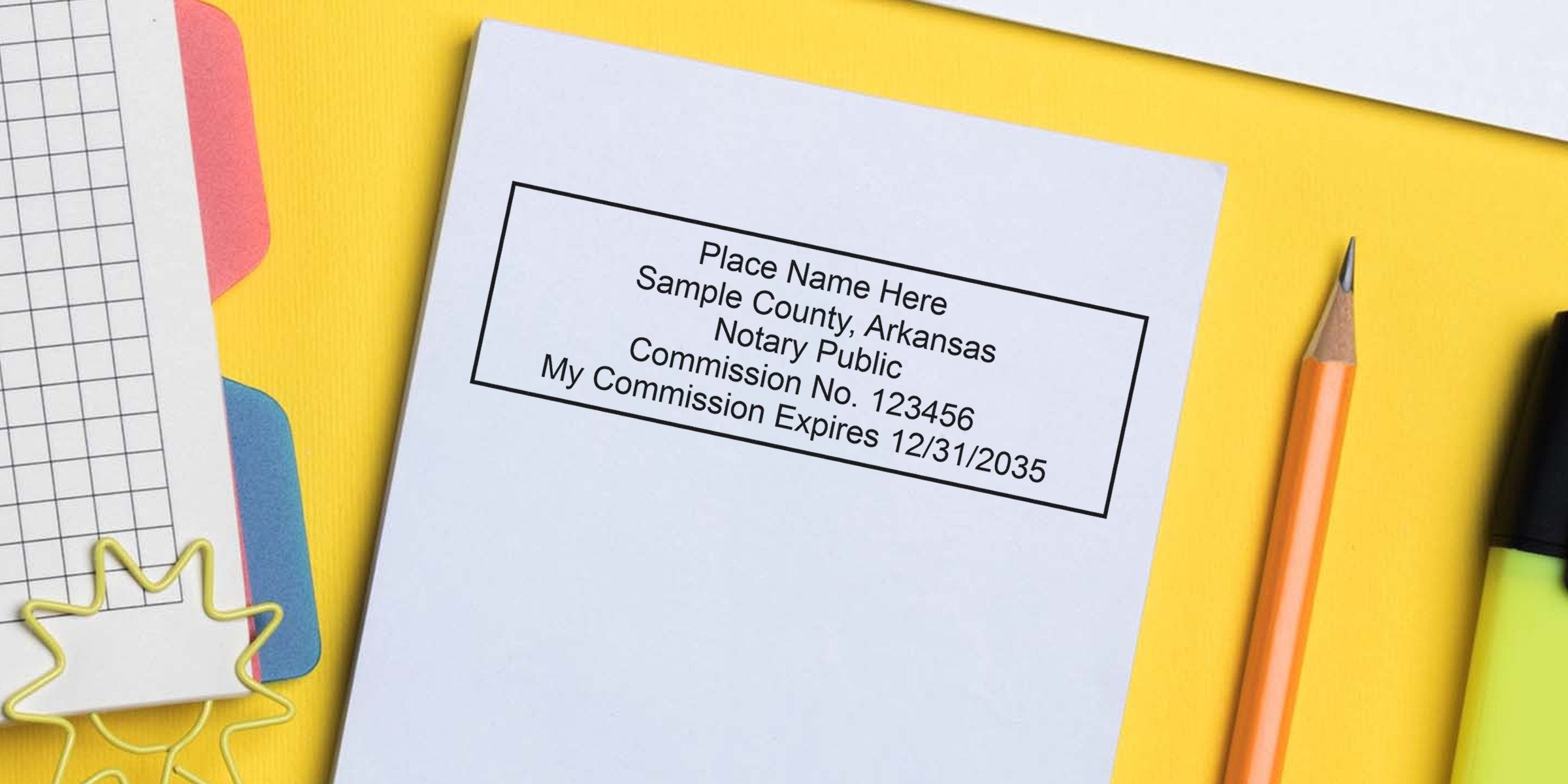 Blank notary stamp sample on white paper reading "Sample County, Arkansas Notary Public Commission No. 123456 My Commission Expires 12/31/2035" with pencil, highlighter and colorful file tabs on a yellow desk background