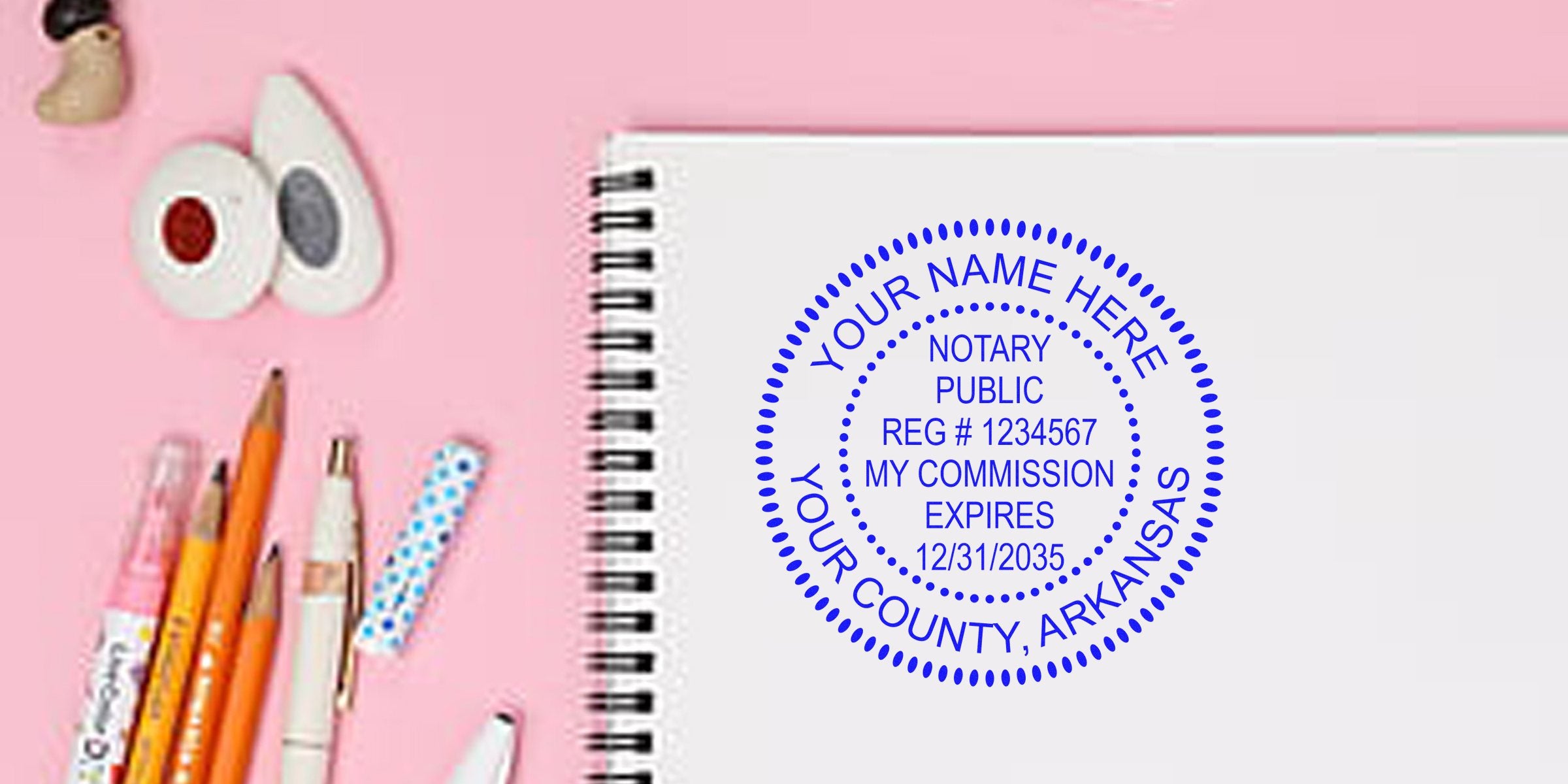 Blue circular notary public stamp mockup on white spiral notebook reading "Your Name Here, Your County, Arkansas" with registration number and commission expiry, on a pink desk with pencils, pens and correction tape.