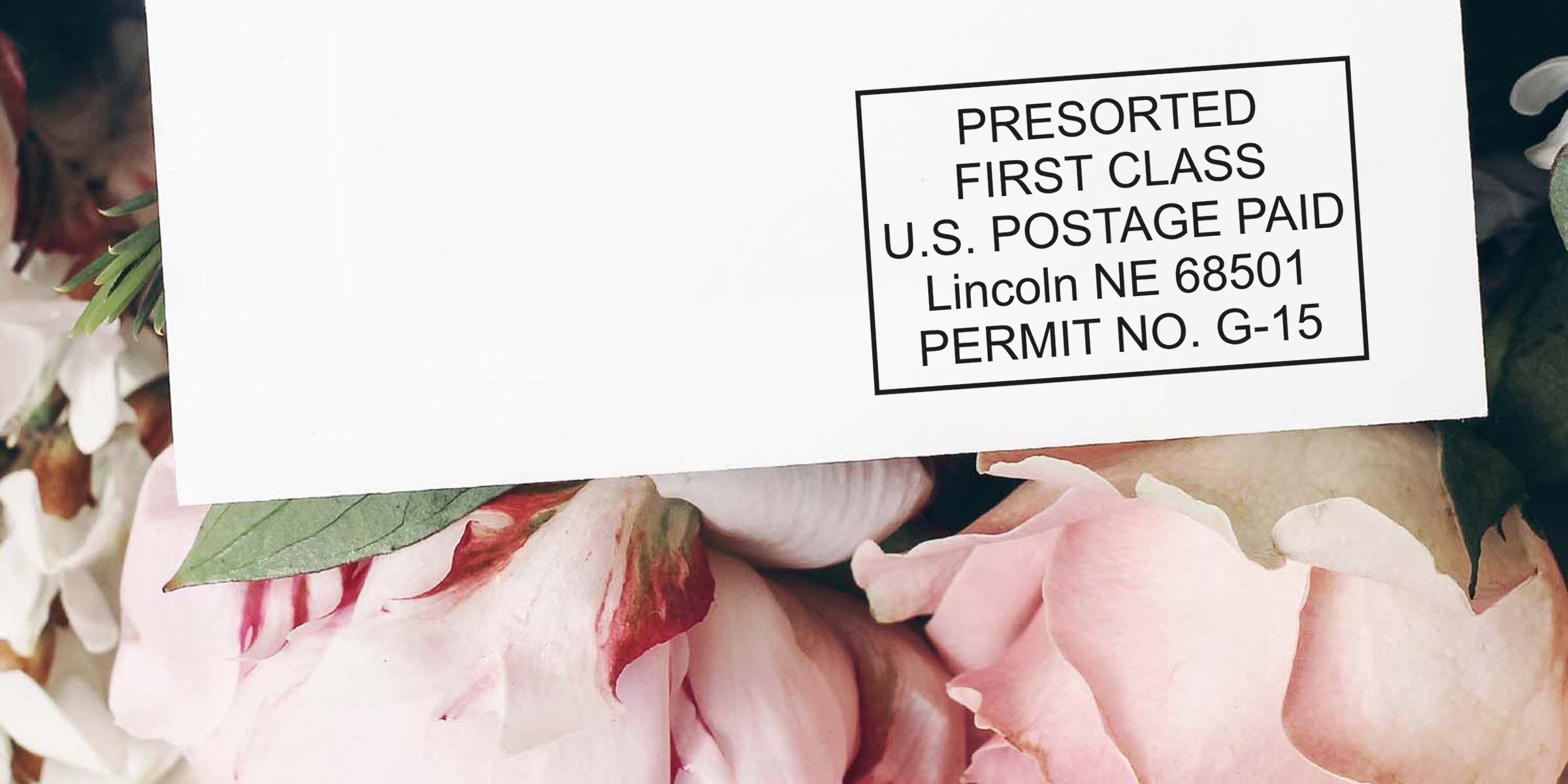 A white card with a black bordered stamp reading “PRESORTED FIRST CLASS U.S. POSTAGE PAID Lincoln NE 68501 PERMIT NO. G-15,” placed among pink flower petals.