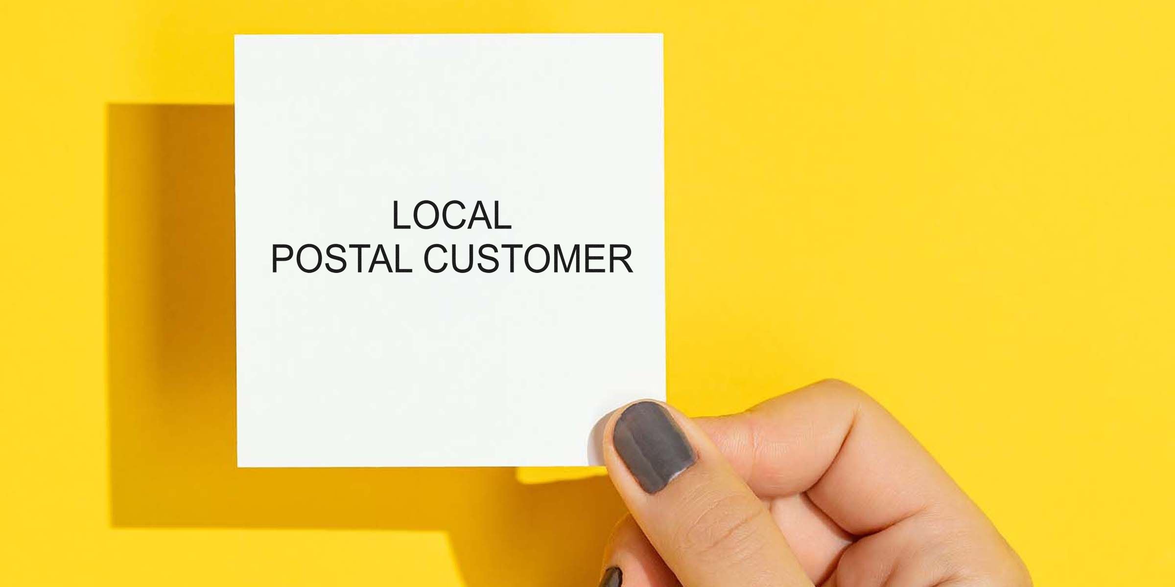 White square card with the words “LOCAL POSTAL CUSTOMER” being held by a hand against a bright yellow background.