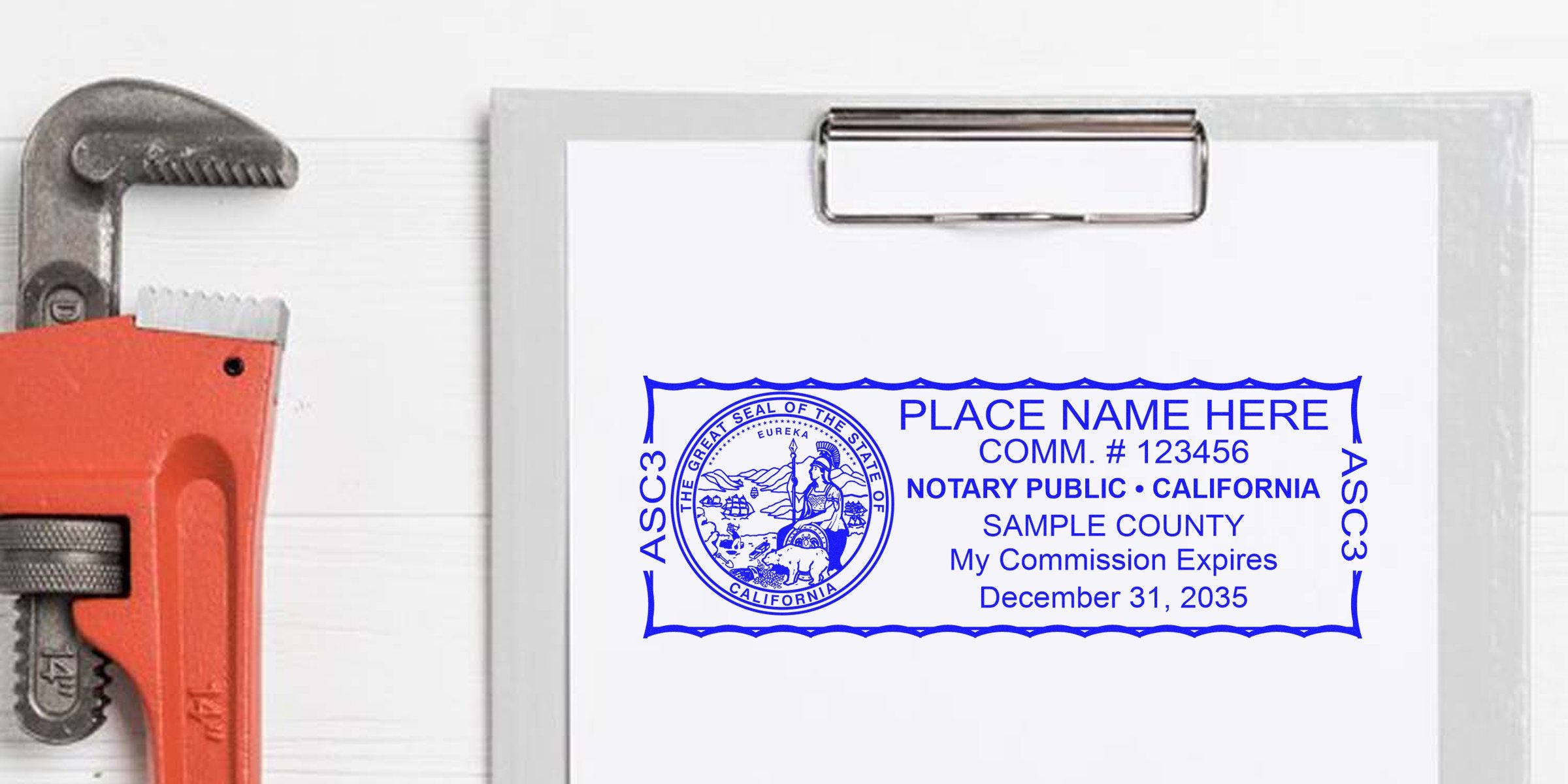 Top-view clipboard with printed blue California notary public stamp sample showing placeholder name, commission number, county and expiration date, beside an orange pipe wrench on a white wooden background