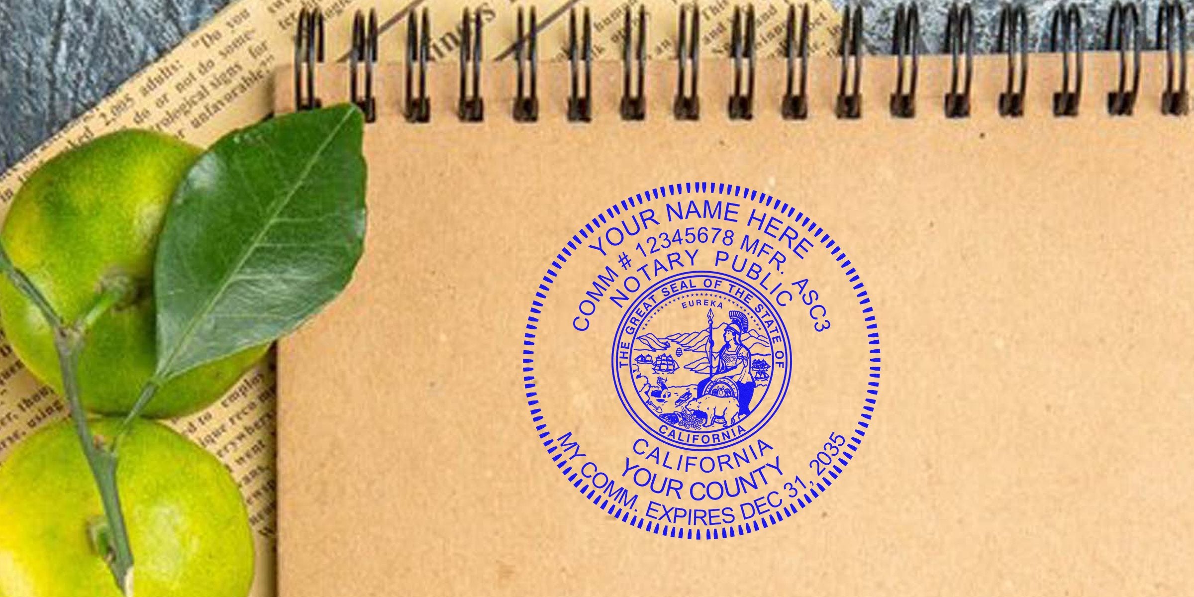Top-down view of a kraft paper spiral notebook with a blue California notary public seal stamped on the page, next to green citrus fruit and leaves.