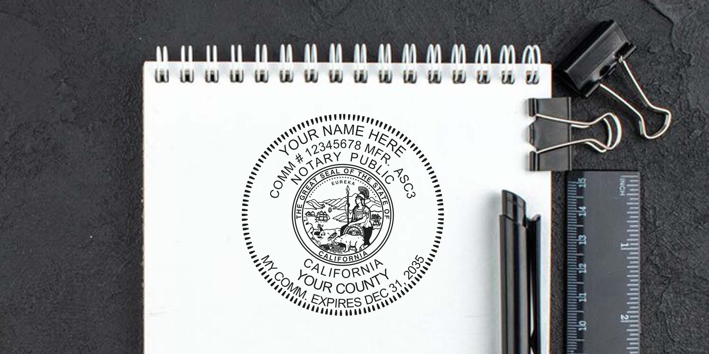 California notary public circular seal stamp mockup on white spiral notebook, with black pens, ruler and binder clips on a dark desk surface