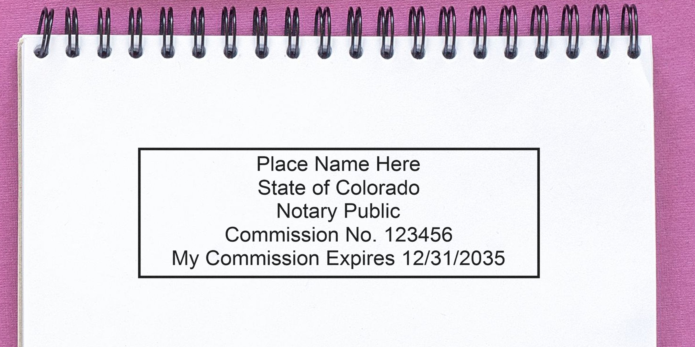 Blank spiral notebook page showing a rectangular Colorado notary stamp sample reading "Place Name Here, State of Colorado, Notary Public, Commission No. 123456, Expires 12/31/2035" on pink background