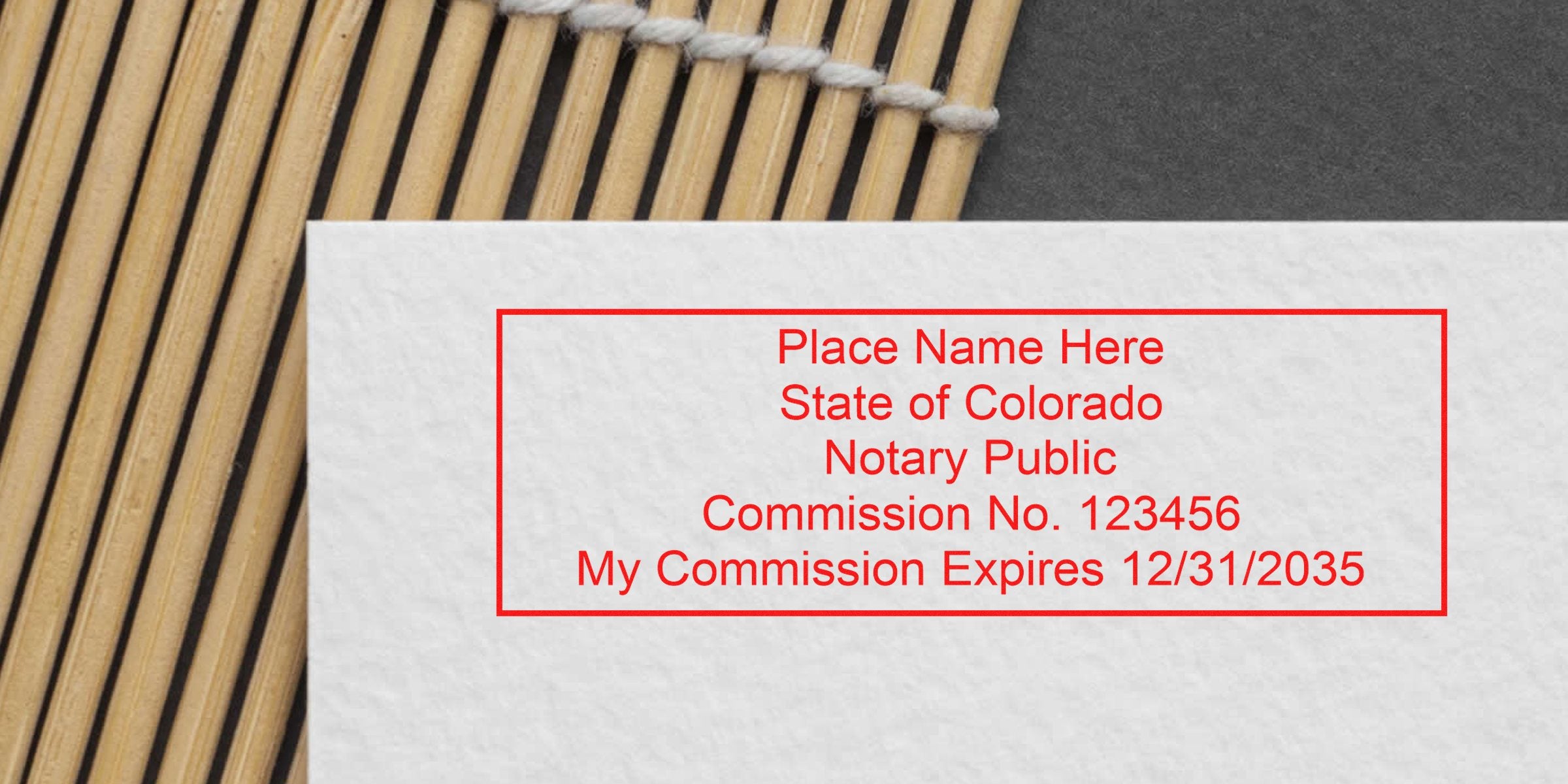Red rectangular notary stamp mockup on textured white paper reading "Place Name Here, State of Colorado, Notary Public, Commission No. 123456, My Commission Expires 12/31/2035" over bamboo mat background