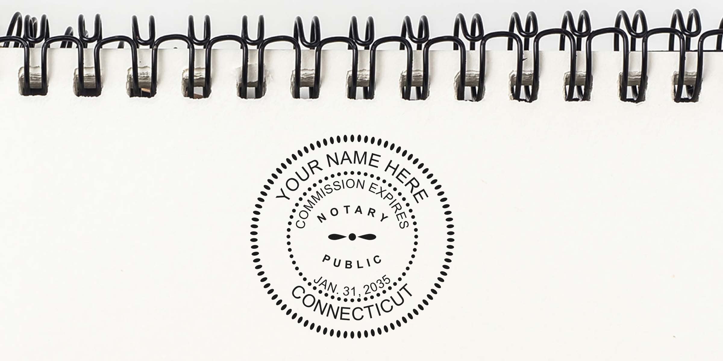 Close-up of black spiral-bound notebook top edge with a round notary public stamp on white paper reading "Your Name Here," "Commission Expires Jan. 31, 2035," and "Connecticut."