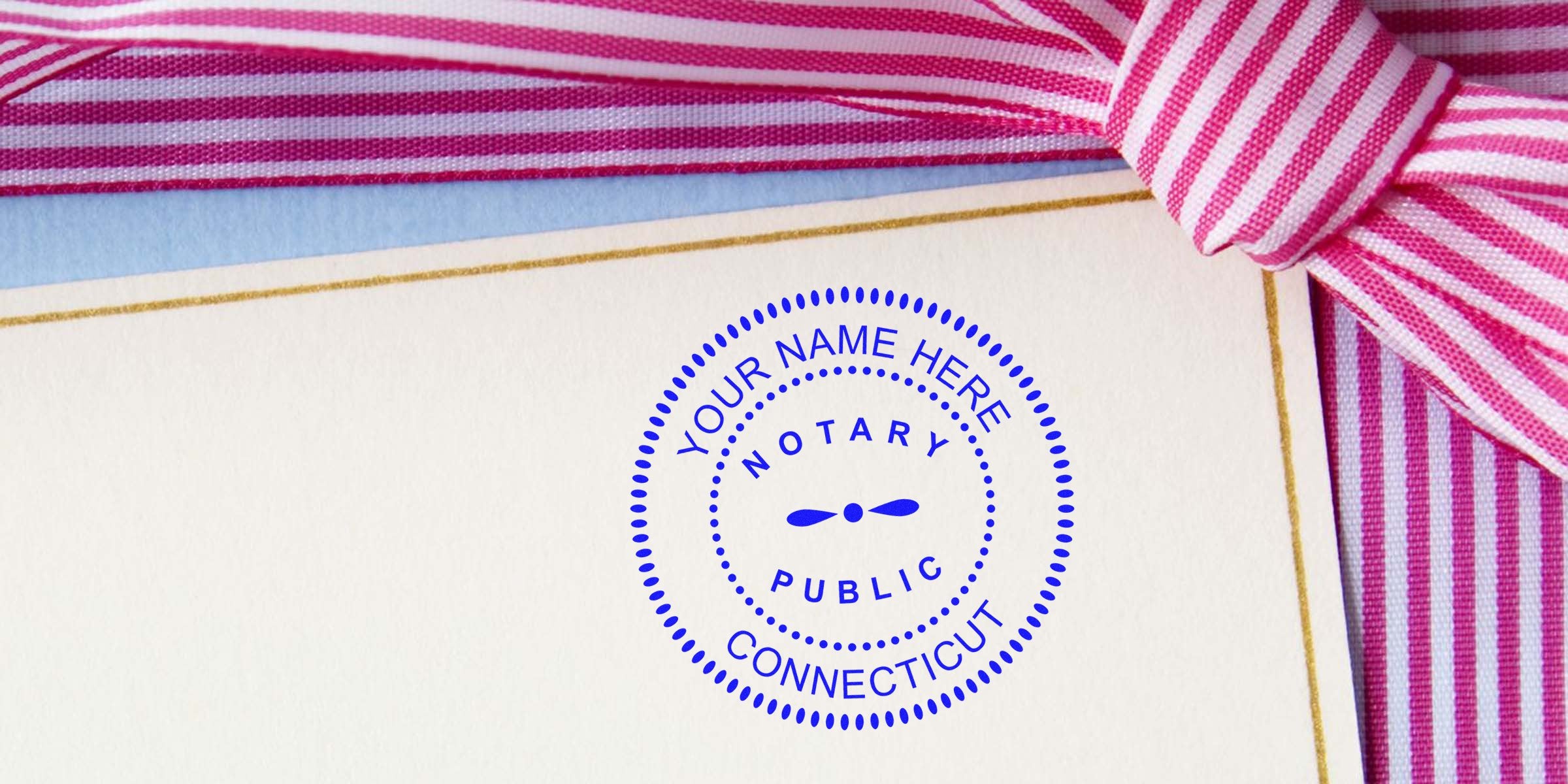 Blue circular notary public stamp reading "Your Name Here, Connecticut" on cream stationery with gold trim, pink striped ribbon bow — customizable Connecticut notary seal for certificates, documents, or gifts