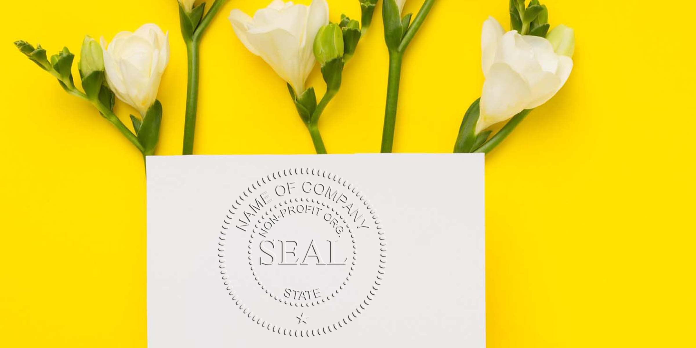 White card with an embossed circular seal reading “SEAL” placed among white flowers on a bright yellow background.