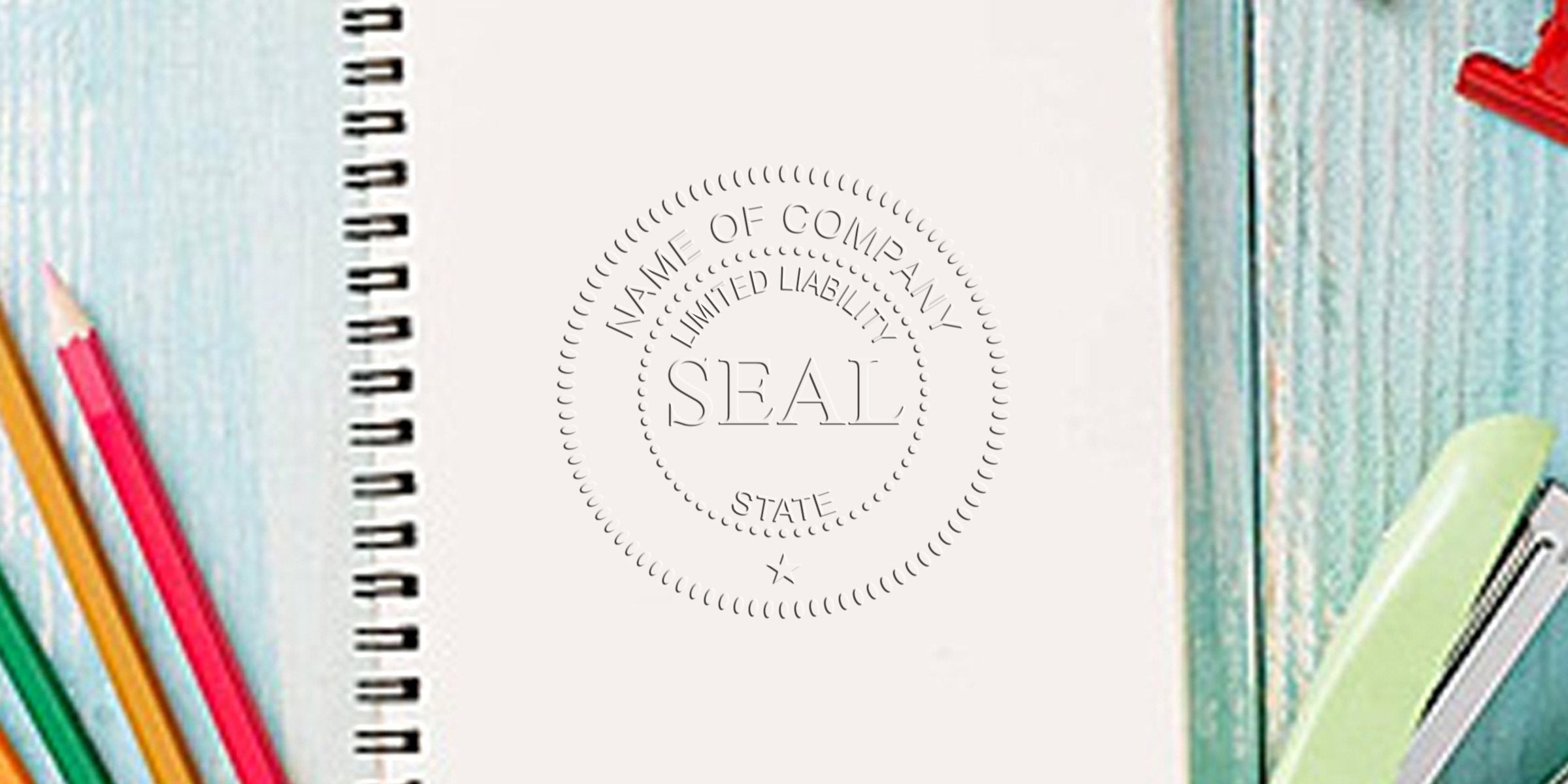 Close-up of a notebook page with a circular SEAL graphic, surrounded by a spiral binding and colorful pencils and stationery.