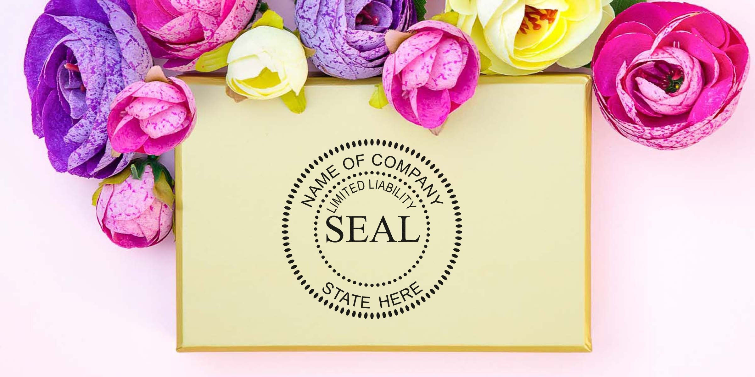 Beige gift box with a black circular seal reading “SEAL” surrounded by a dotted ring, placed among bright pink, purple, and yellow flowers on a pale pink background.