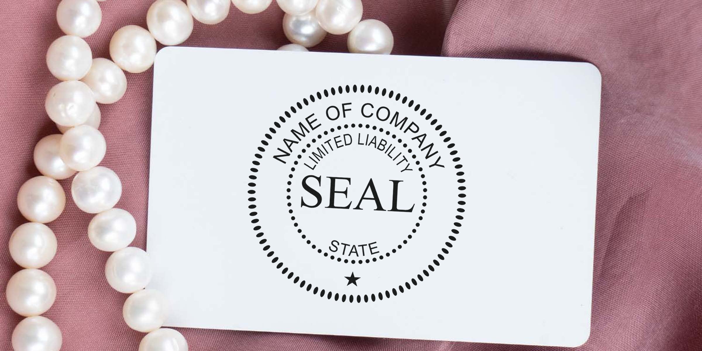 SEAL stamp design on a white card with dotted circular borders, surrounded by a pearl necklace on pink fabric.
