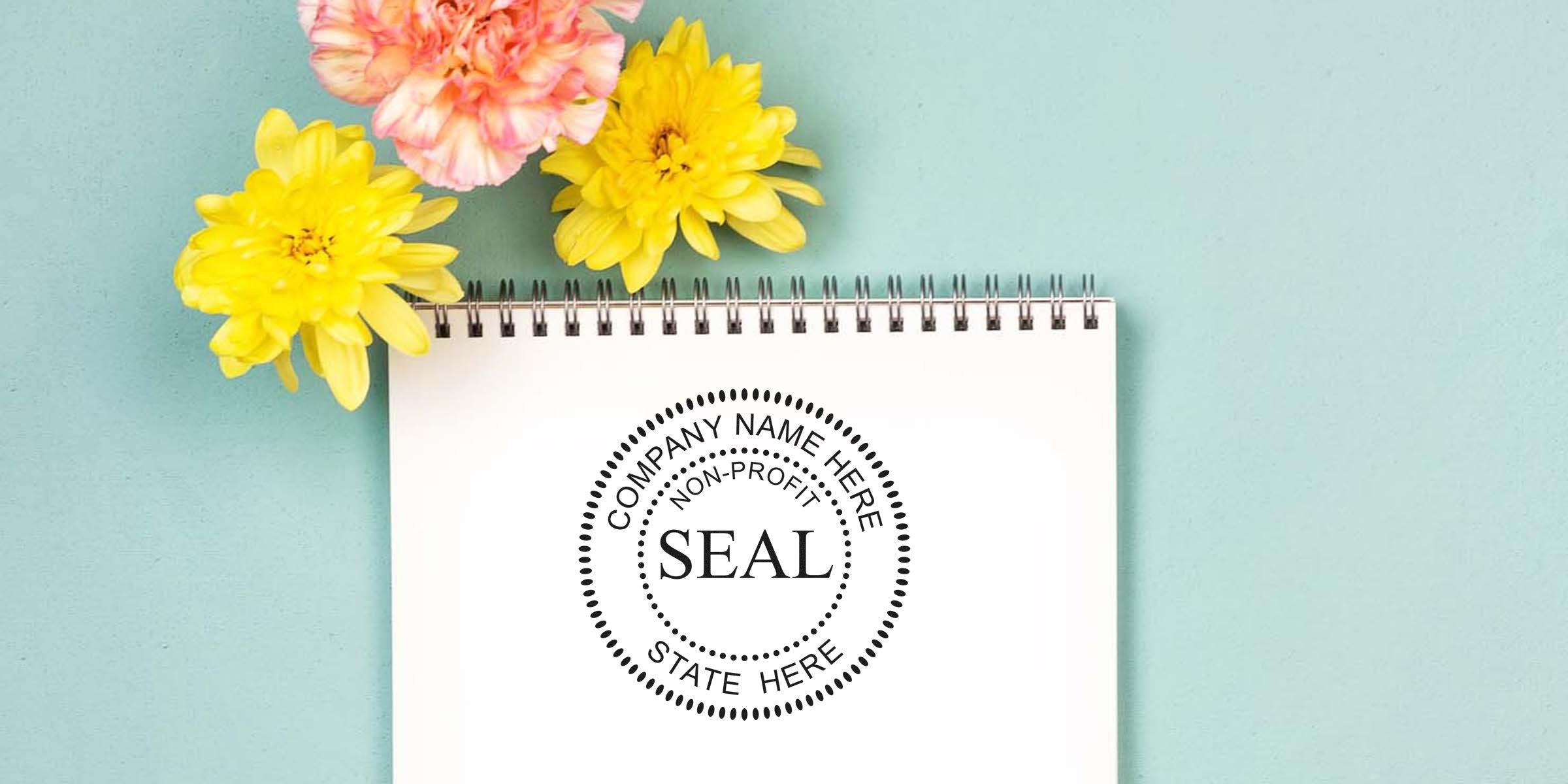 Spiral notebook page featuring a circular “SEAL” stamp design with decorative text, beside yellow and pink flowers on a teal background.