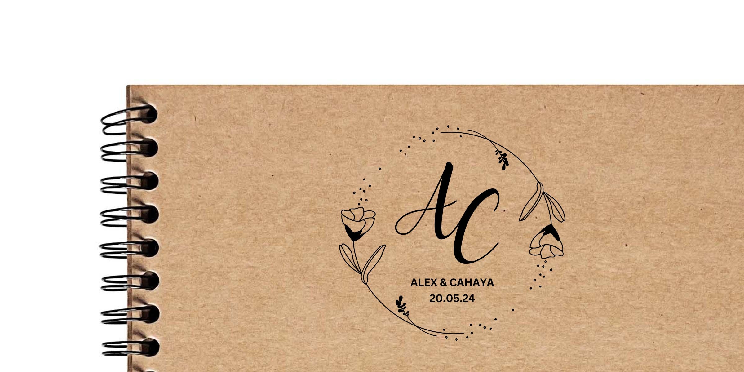 Kraft spiral-bound notebook cover with black floral wreath logo featuring large initials "AC", names "Alex & Cahaya" and date "20.05.24" centered on textured brown paper