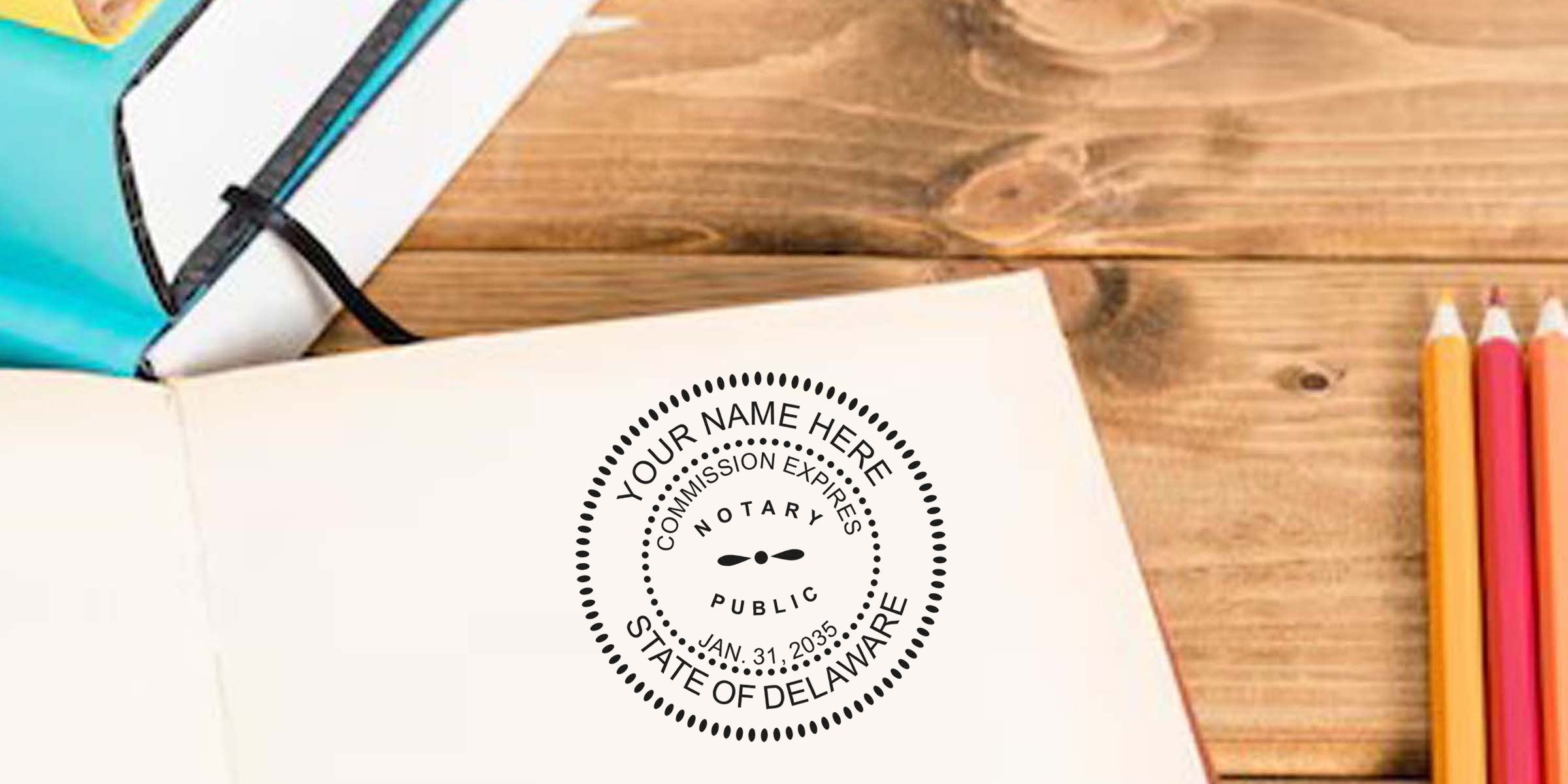 Open notebook on wooden desk with circular "Notary Public State of Delaware" stamp impression, colored pencils and teal pencil case nearby