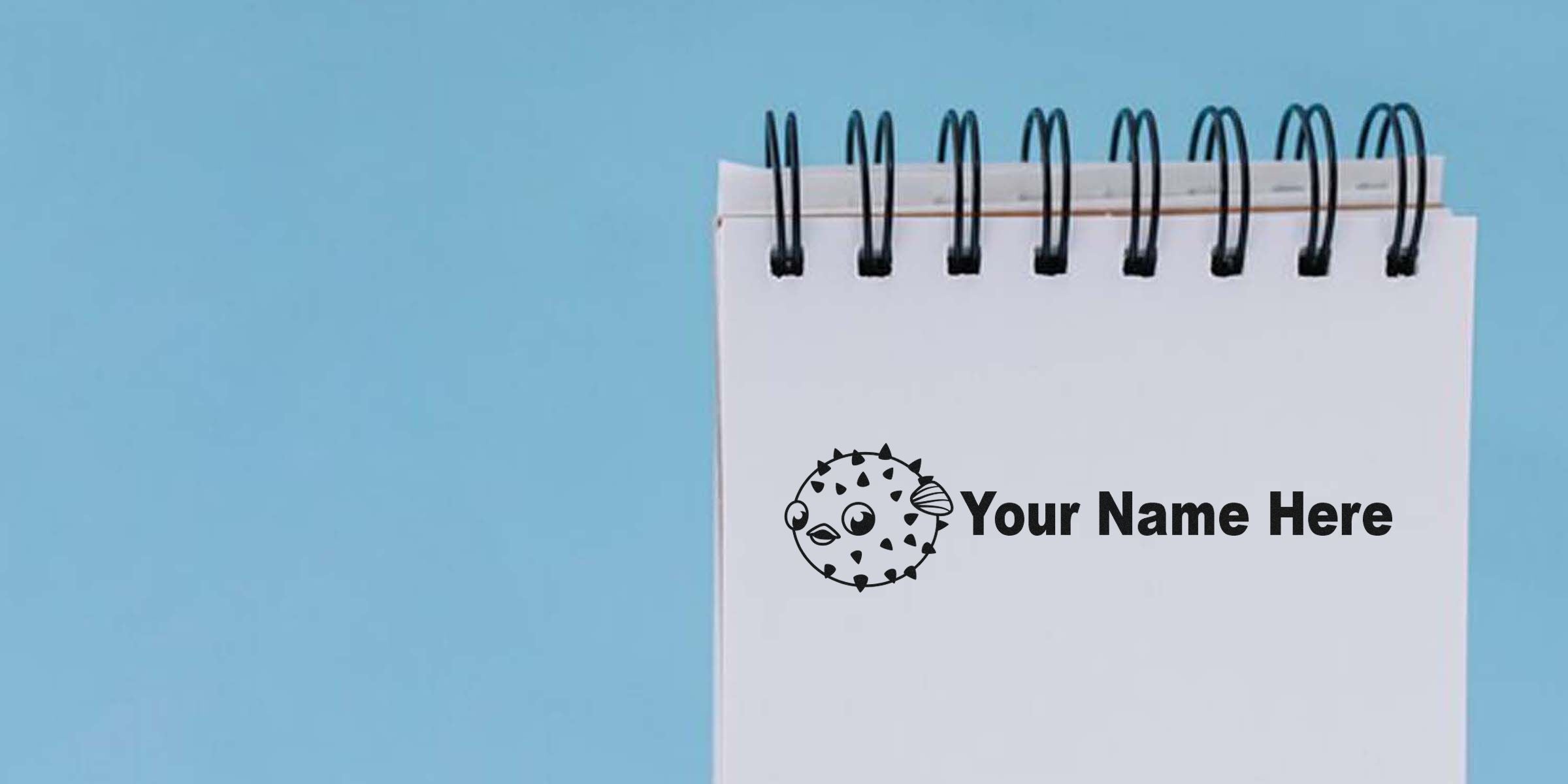 Spiral notebook page with the text “Your Name Here” and a cartoon pufferfish on a blue background.