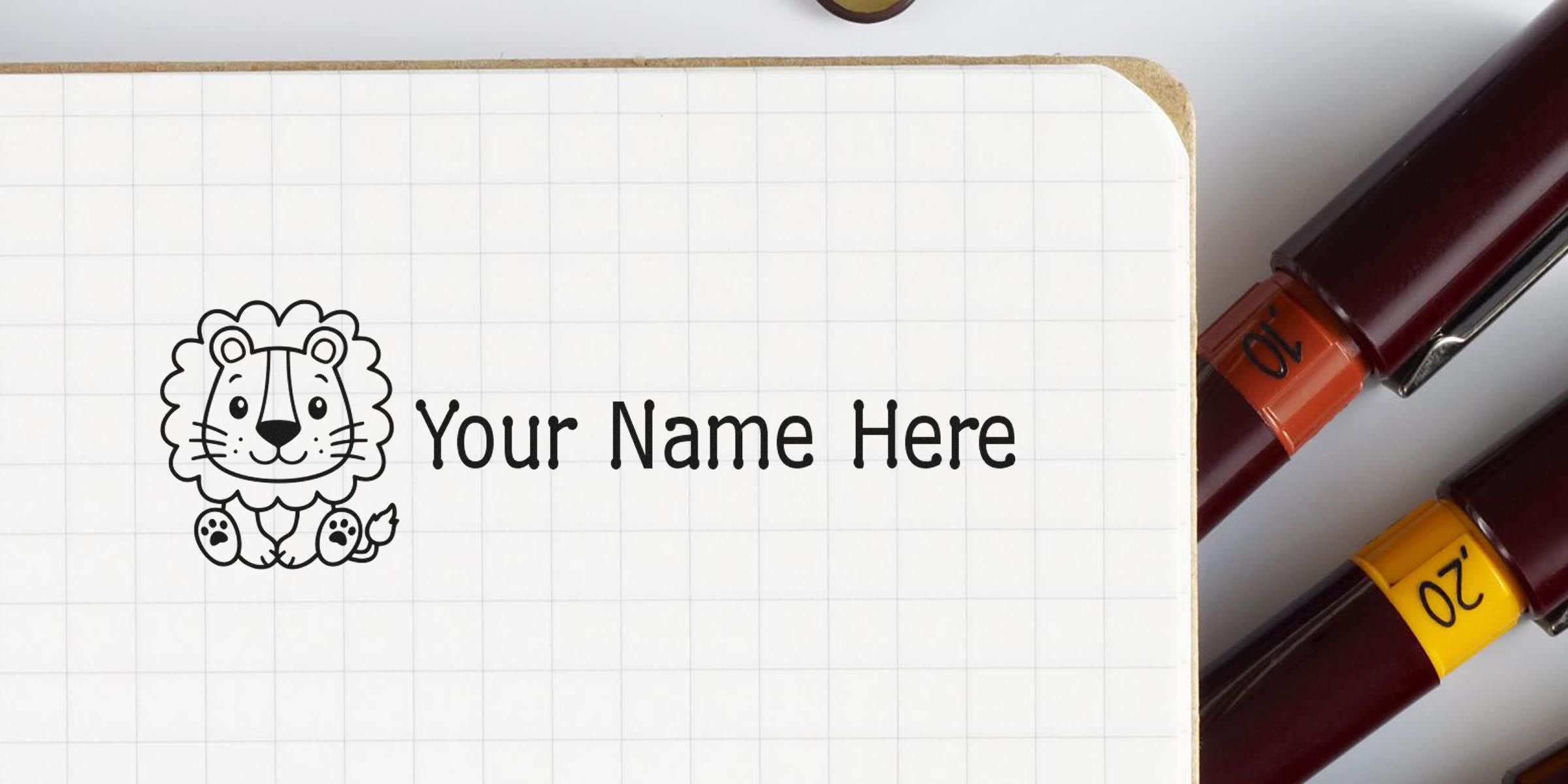 Illustration of a cute lion drawing beside the text “Your Name Here” on a grid notebook with two colored marker pens nearby.