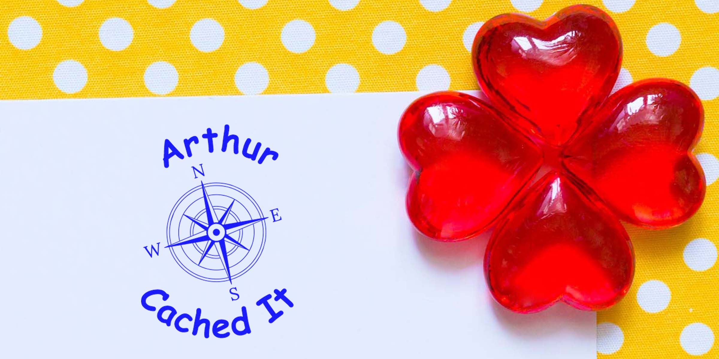 Illustration of a white card with a blue compass rose and the text “Arthur Cached It,” next to a red glass flower on a yellow polka-dot background.