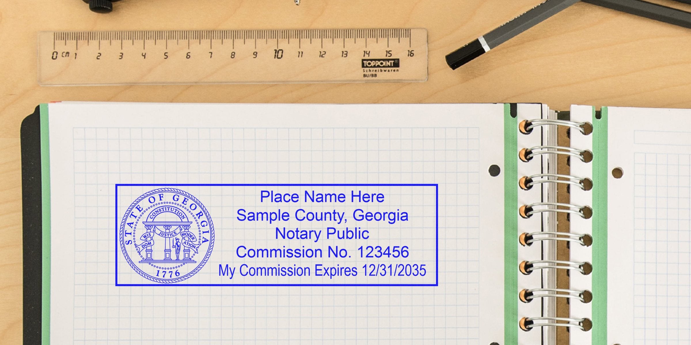 Blue Georgia notary public stamp mockup on graph paper notebook page with spiral binding, ruler and pen on wooden desk showing sample commission number and expiration date.