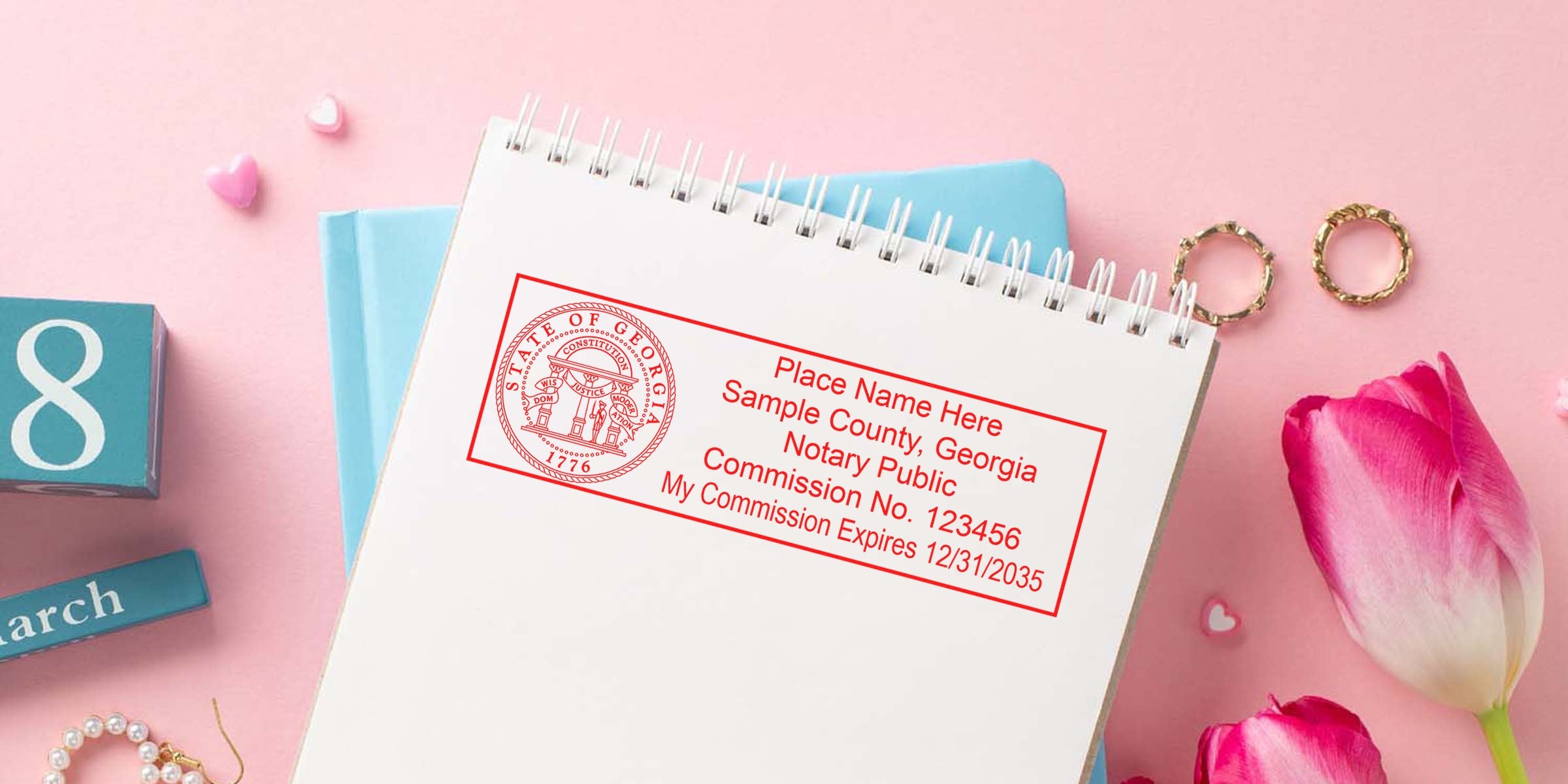 Red Georgia notary public stamp imprint on a spiral notebook flatlay with pink tulips, gold rings, pearl bracelet and a blue March calendar block — feminine legal stationery image for notary services and appointment booking.