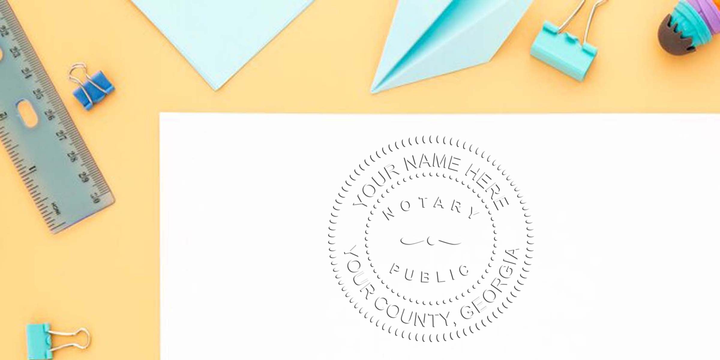 Flat lay of pastel office supplies (ruler, binder clips, paper airplane) on peach background with white paper showing a circular notary public embossing seal for county, Georgia.