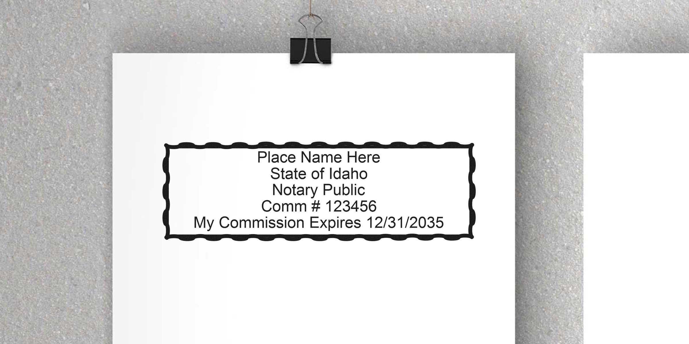 Blank Idaho notary public stamp template printed on white paper clipped to a gray textured wall, showing placeholder name, commission number and expiration date 12/31/2035.