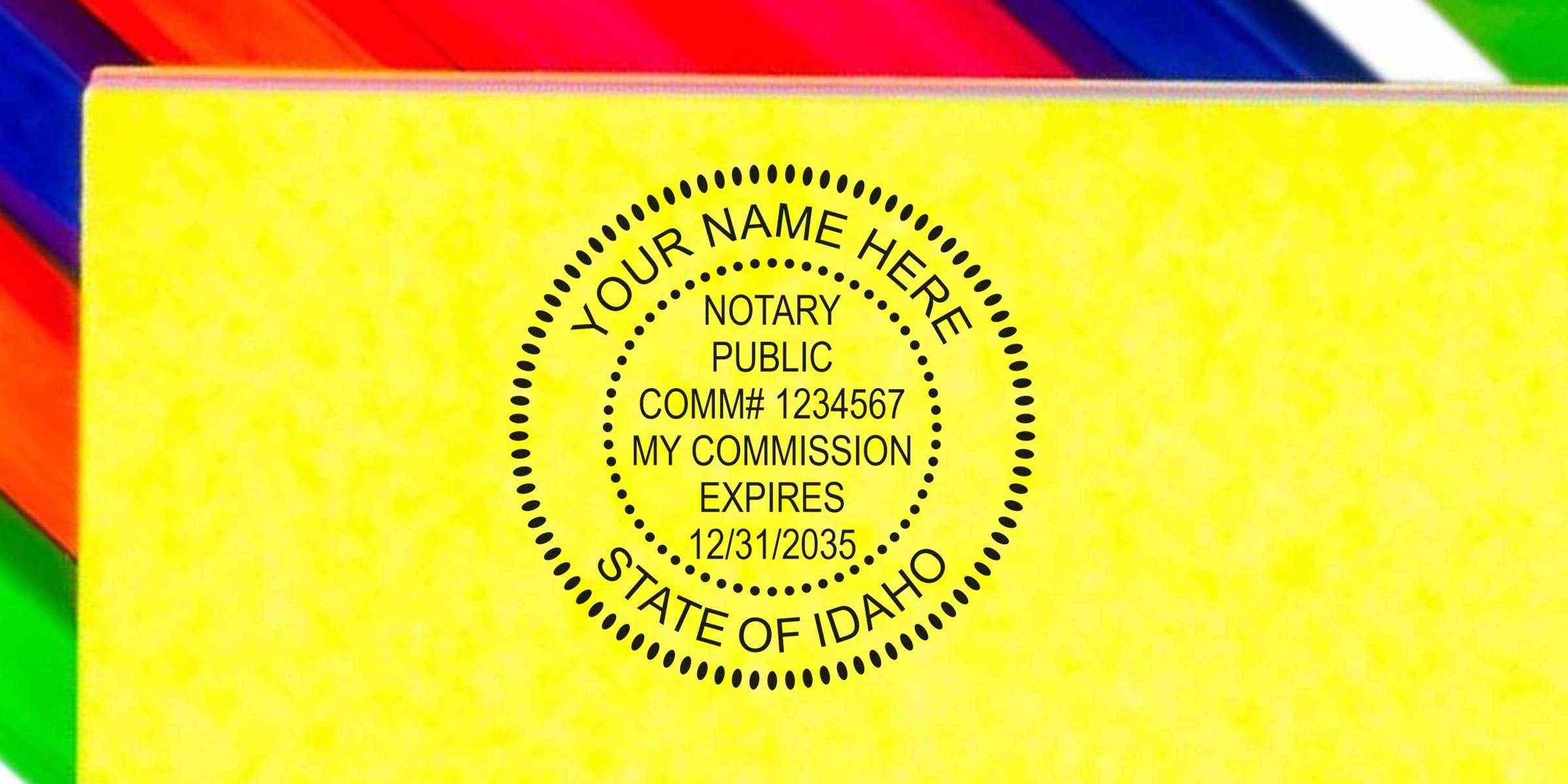 Round Idaho notary public rubber stamp impression on yellow paper reading "Your Name Here, Notary Public, Comm# 1234567, My Commission Expires 12/31/2035" inside dotted circular border, with colorful paper edge visible.