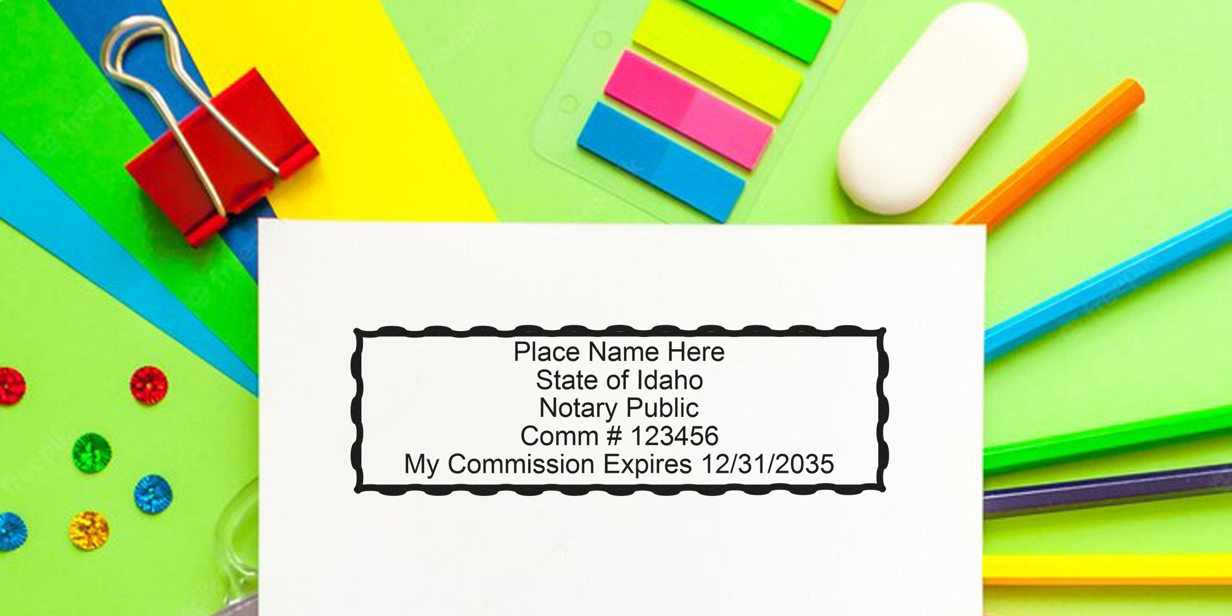 Blank notary stamp sample on white paper reading Place Name Here State of Idaho Notary Public Comm #123456 My Commission Expires 12/31/2035, surrounded by colorful office supplies, sticky tabs, eraser and binder clip.