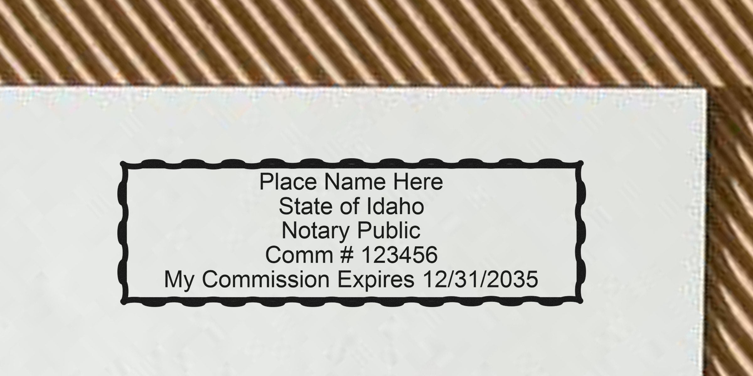 Rectangular scalloped notary stamp template on paper reading "Place Name Here · State of Idaho Notary Public · Comm #123456 · My Commission Expires 12/31/2035" with textured background and diagonal striped border