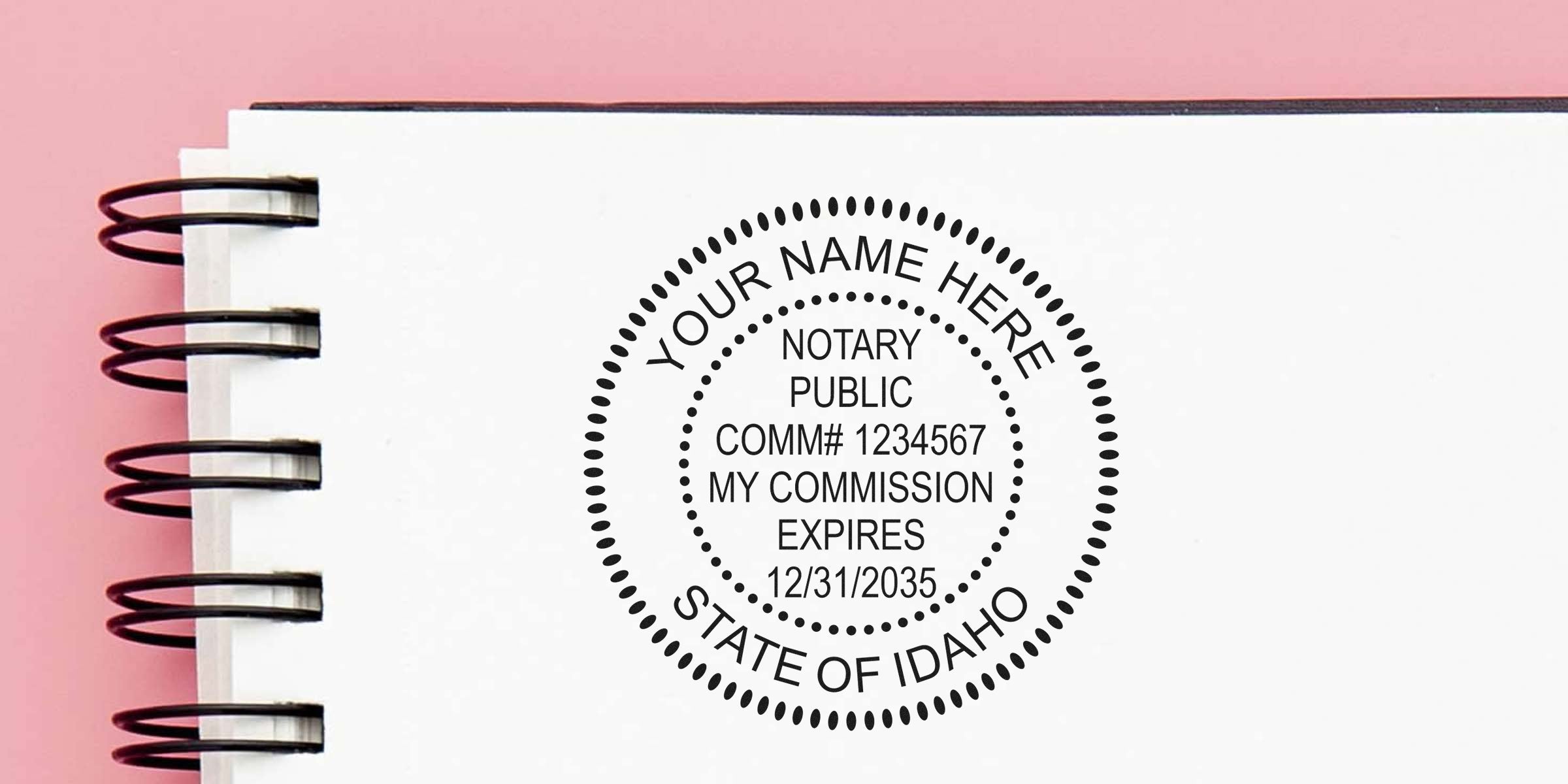 Spiral-bound notebook with black circular notary public seal reading "Your Name Here, State of Idaho" with sample commission number and expiration date on a white page against a pink background