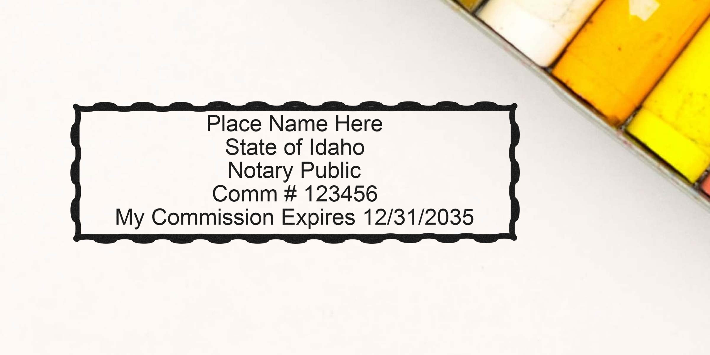 Notary stamp template on white paper with scalloped rectangular border reading "Place Name Here, State of Idaho Notary Public, Comm #123456, My Commission Expires 12/31/2035," with yellow chalks at top-right.