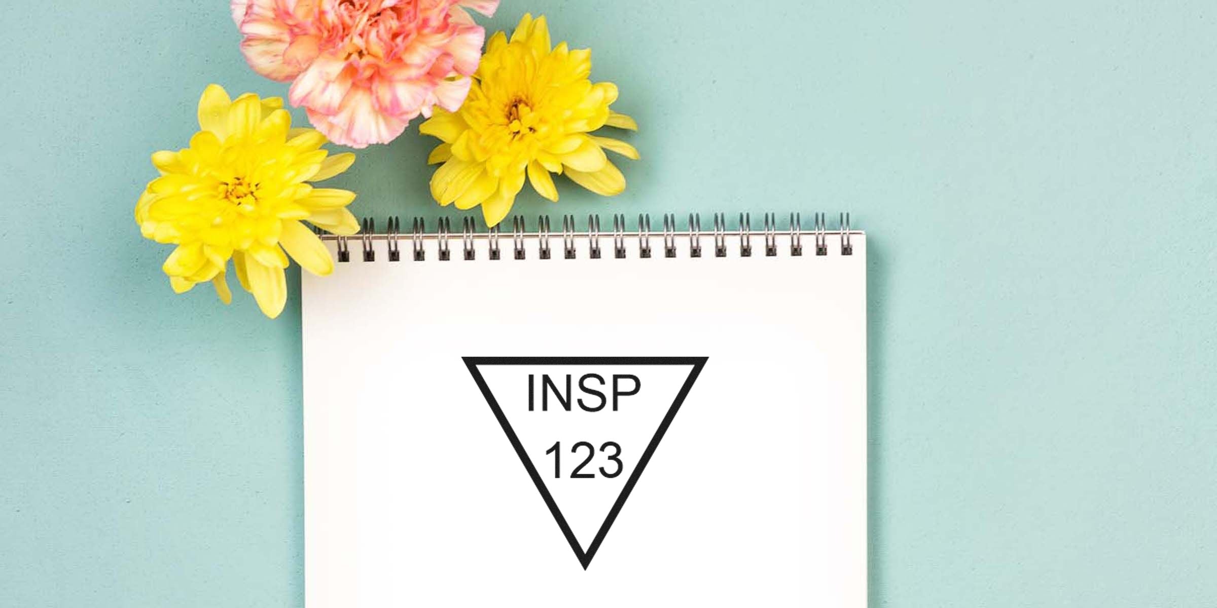 Notebook with a black triangle logo containing the text “INSP 123” and yellow flowers on a teal background.