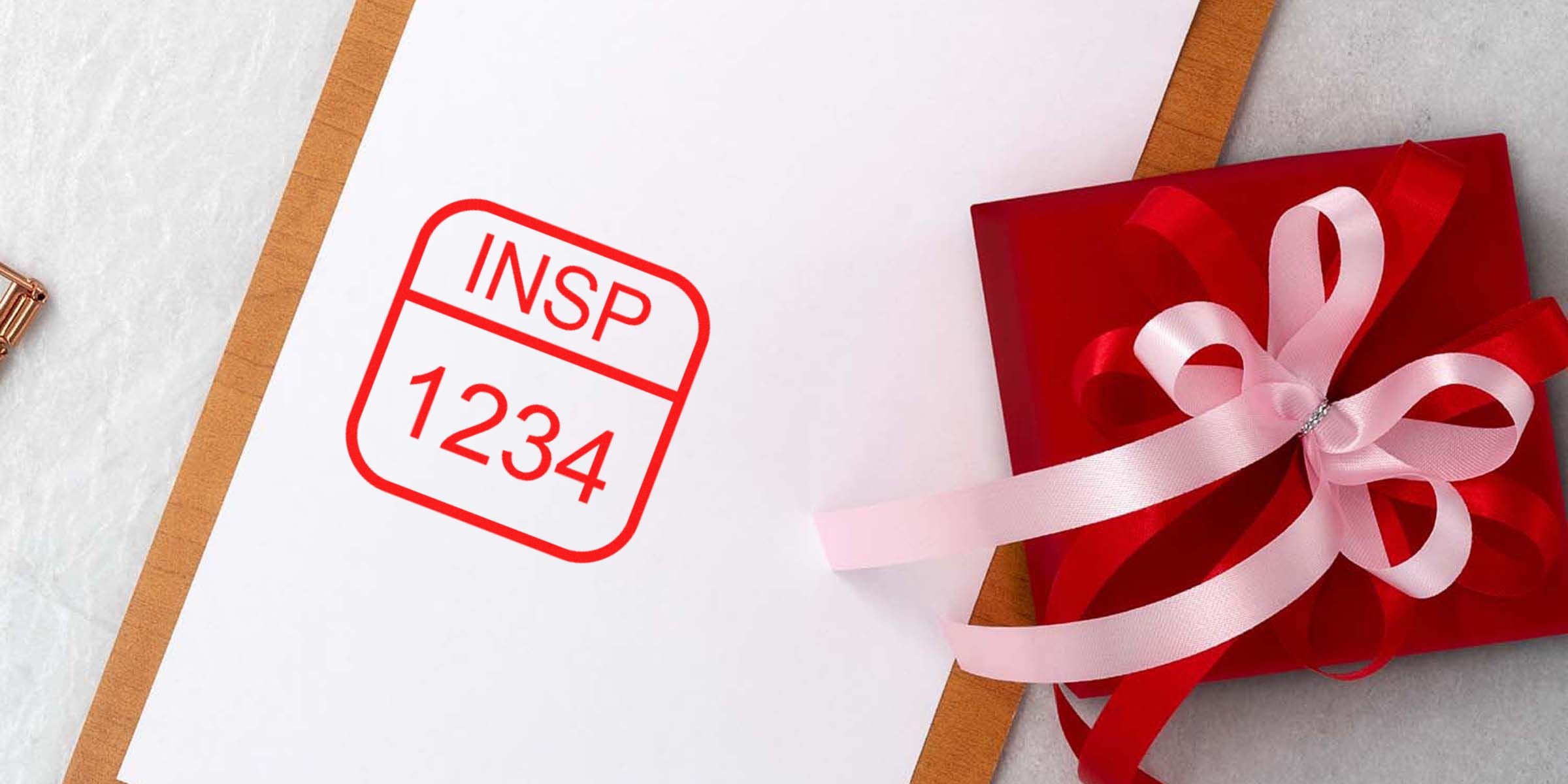 Red gift box with pink ribbon beside a white surface stamped with a red "INSP 1234" label.