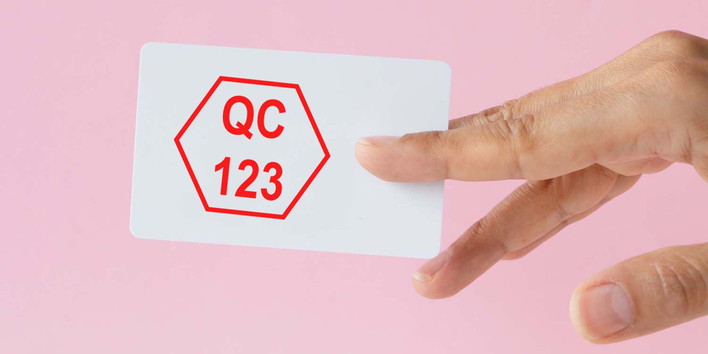 A hand holding a white card with a red hexagon and the text “QC 123” on a pink background.