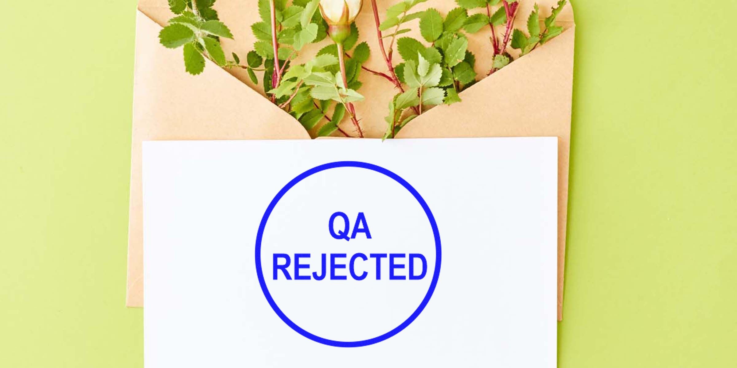 White card with a blue "QA REJECTED" stamp placed over a brown envelope on a green background.