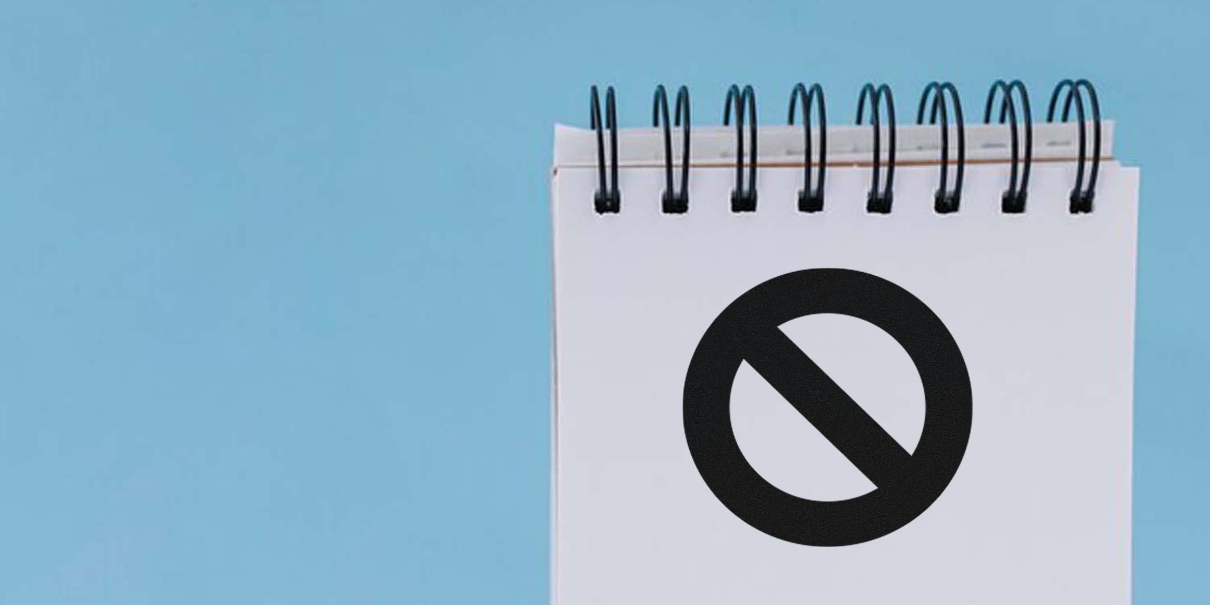 Close-up of a white spiral-bound notebook page with a large black no/no-entry symbol on a light blue background.