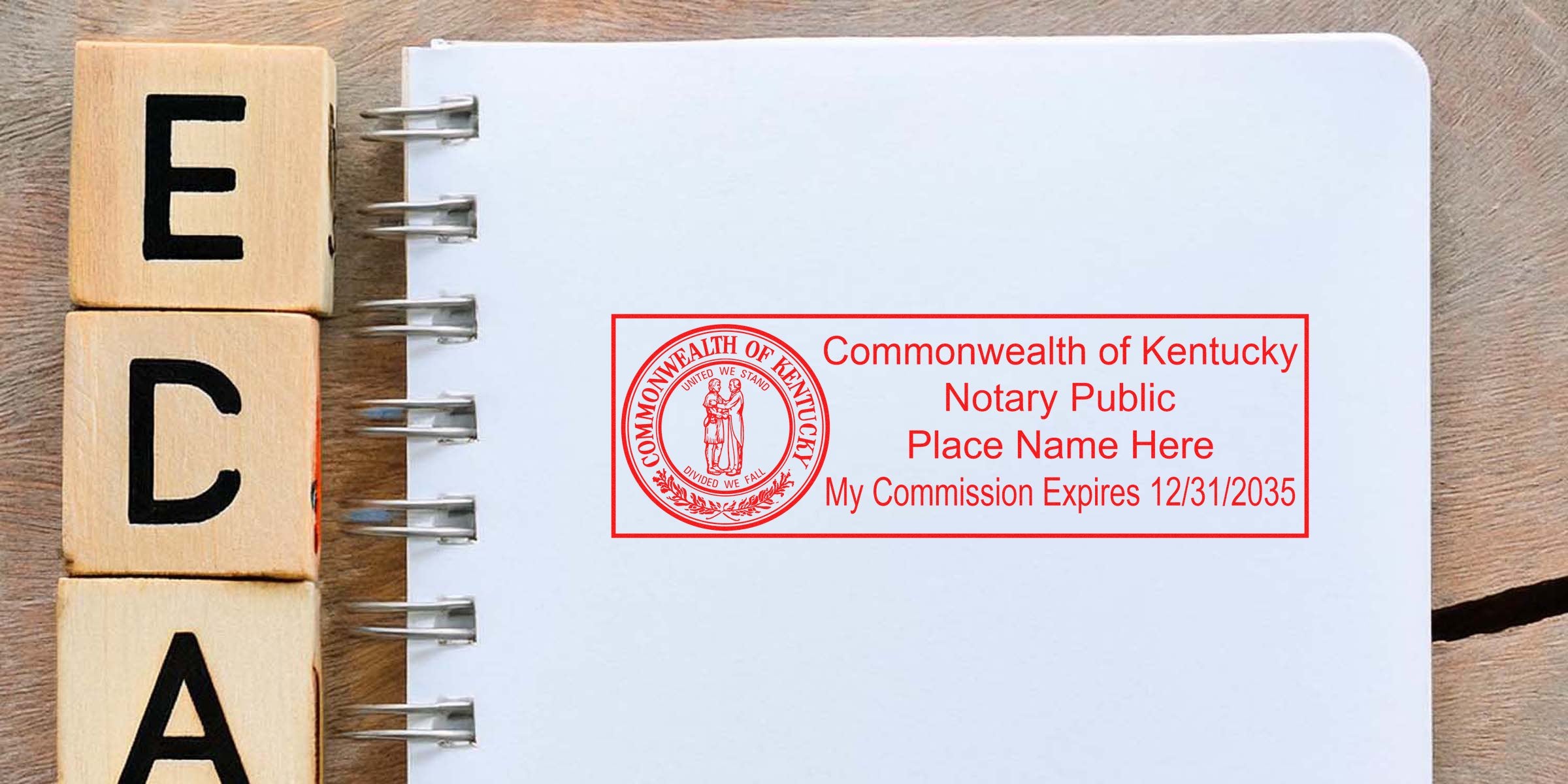 Red Commonwealth of Kentucky notary public stamp impression with blank "Place Name Here" and commission expiration date on white spiral notebook beside wooden letter blocks.