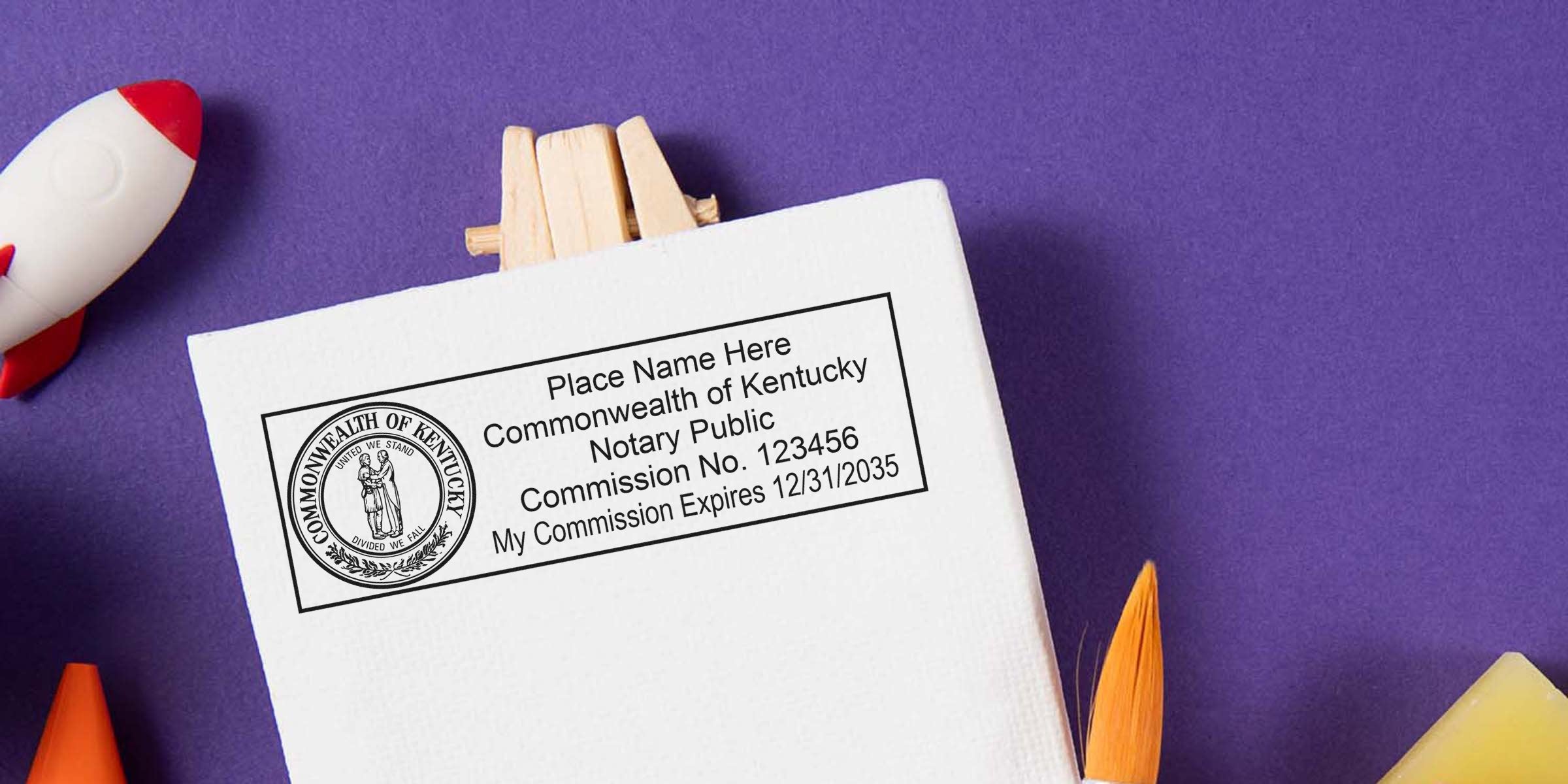 Mockup of Commonwealth of Kentucky notary public stamp on white canvas showing placeholder name, Commission No. 123456 and expiration 12/31/2035, on purple background with toy rocket and paintbrush accents.