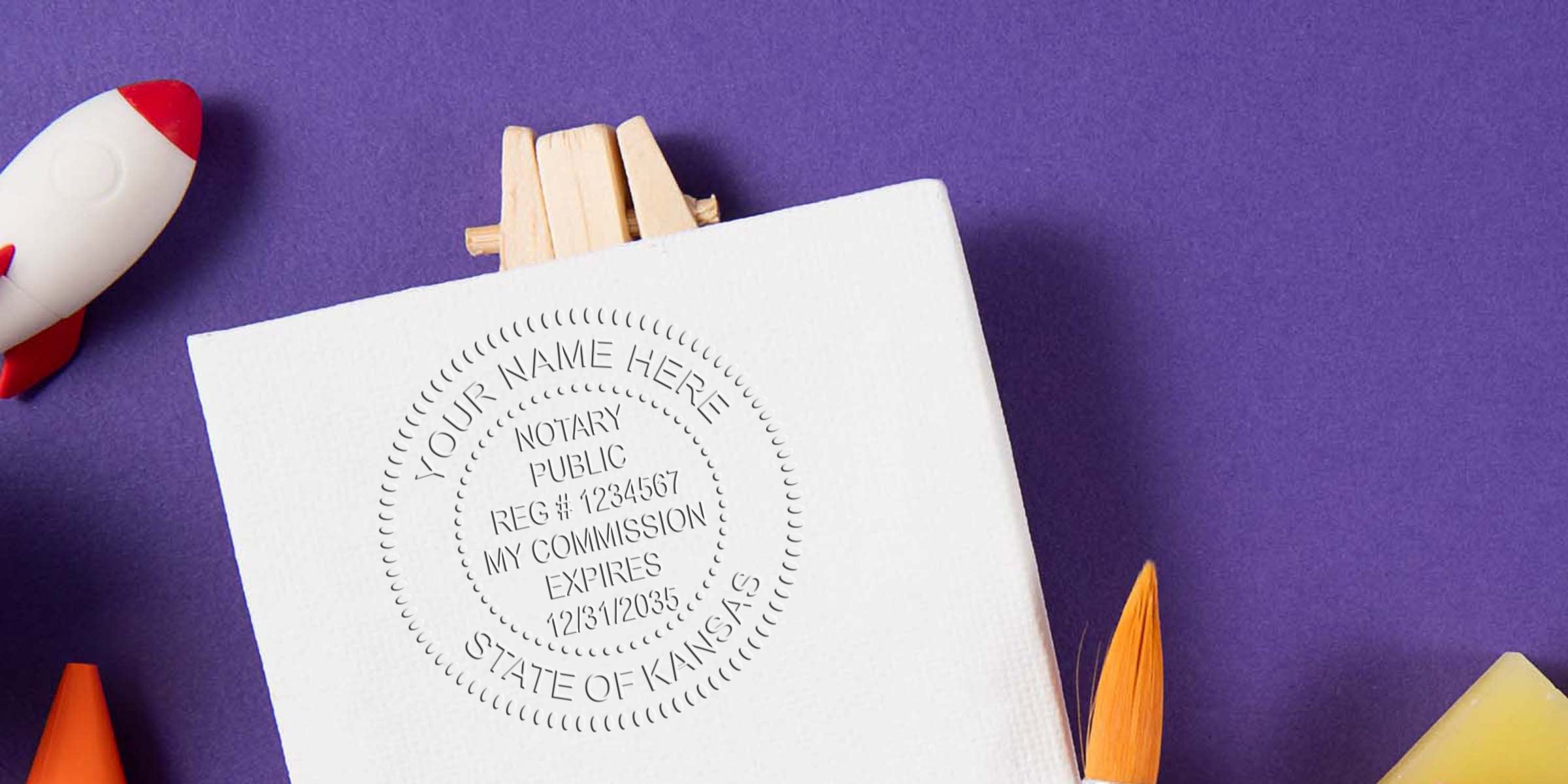 Embossed notary public seal on white cardstock (State of Kansas) on purple background with toy rocket and paintbrush — notary seal embossing, stationery, craft props