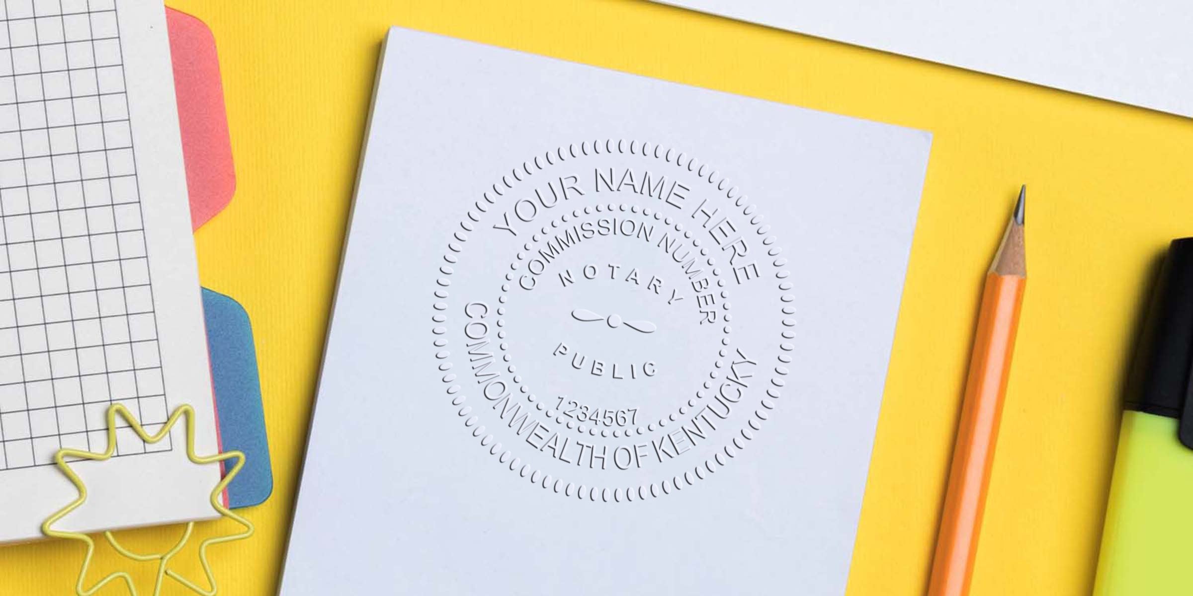 Embossed notary public seal on white document reading "Commonwealth of Kentucky" and placeholder name, photographed on yellow desk with pencil, highlighter and grid notebook — notary seal office supplies photo