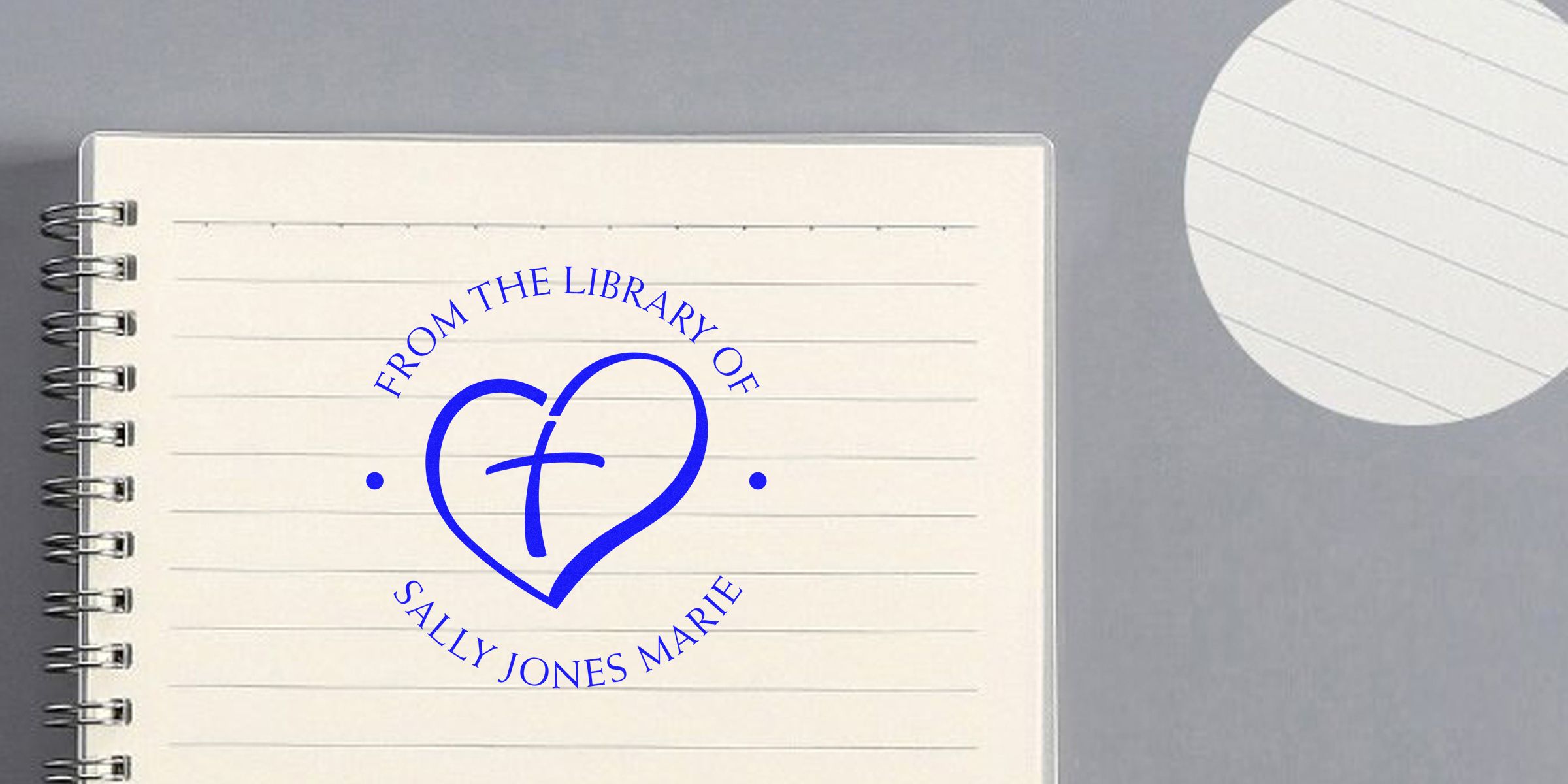 Blue circular stamp on a spiral notebook that reads “FROM THE LIBRARY OF SALLY JONES MARIE” surrounding a heart with a stylized “f.”