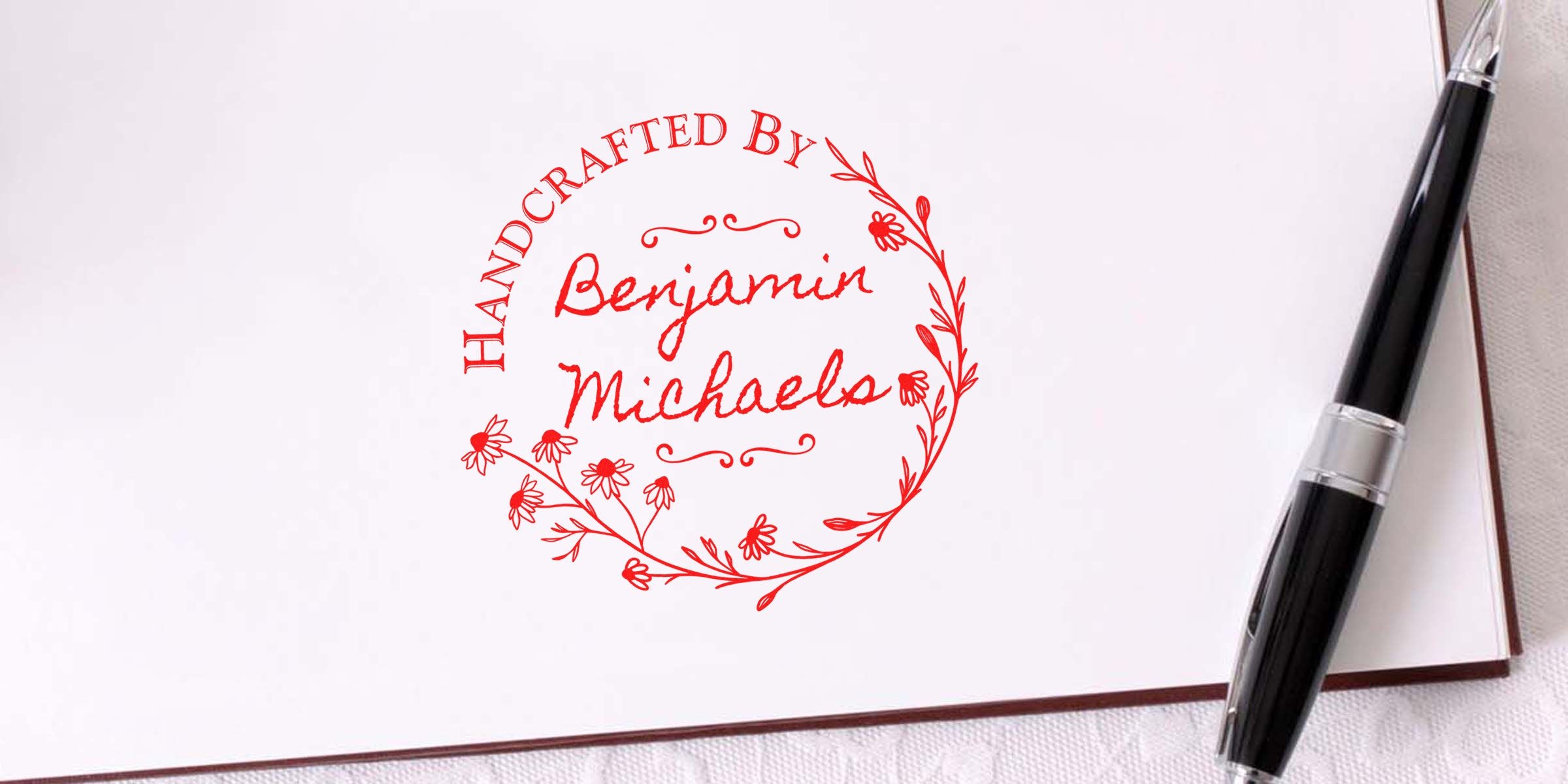 Red circular stamp reading "Handcrafted by Benjamin Michaels" with floral border on white paper, beside a black pen.