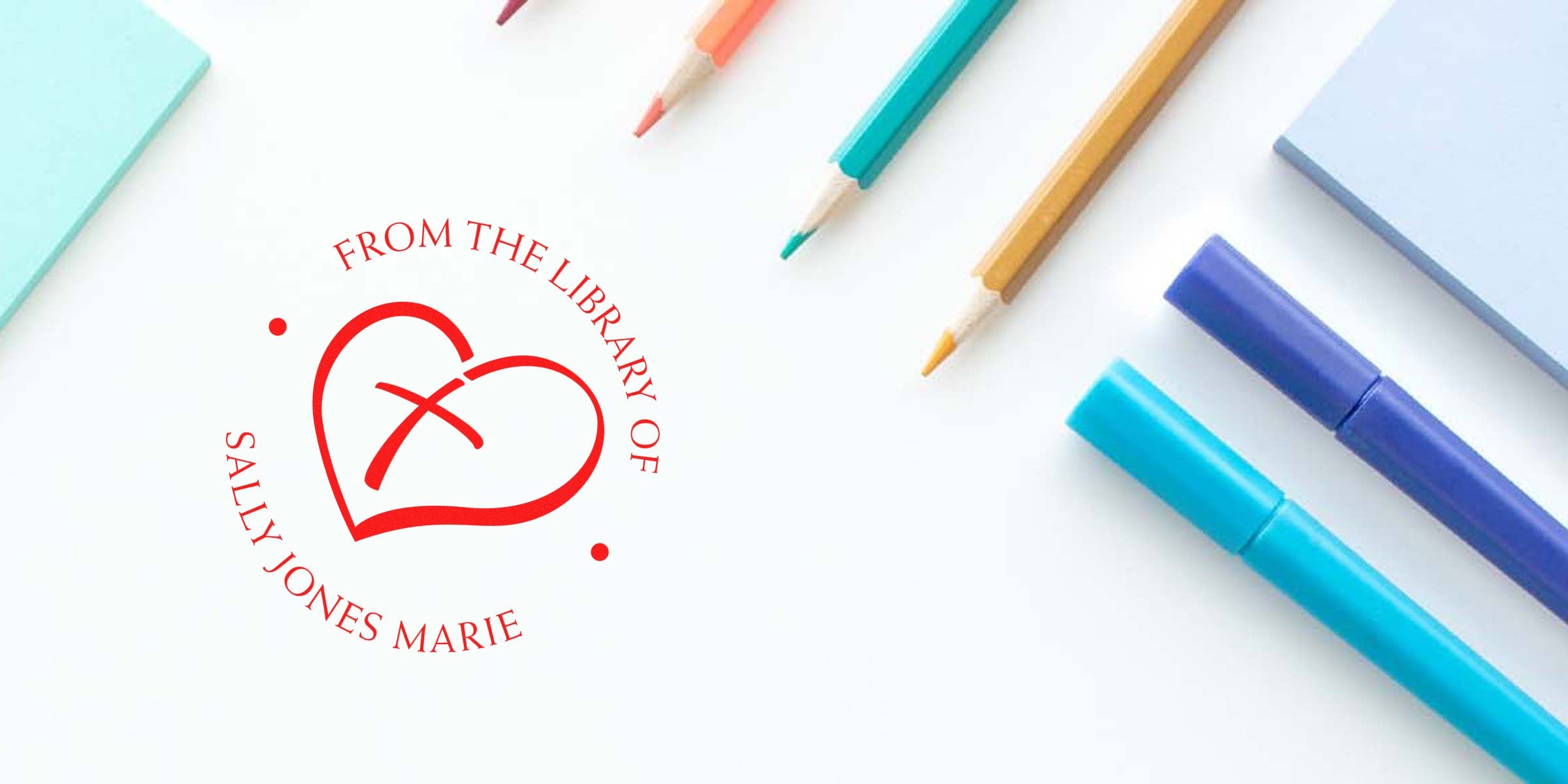 Red heart logo with circular text reading “FROM THE LIBRARY OF SALLY JONES MARIE” on a white surface, surrounded by colorful pencils and markers.