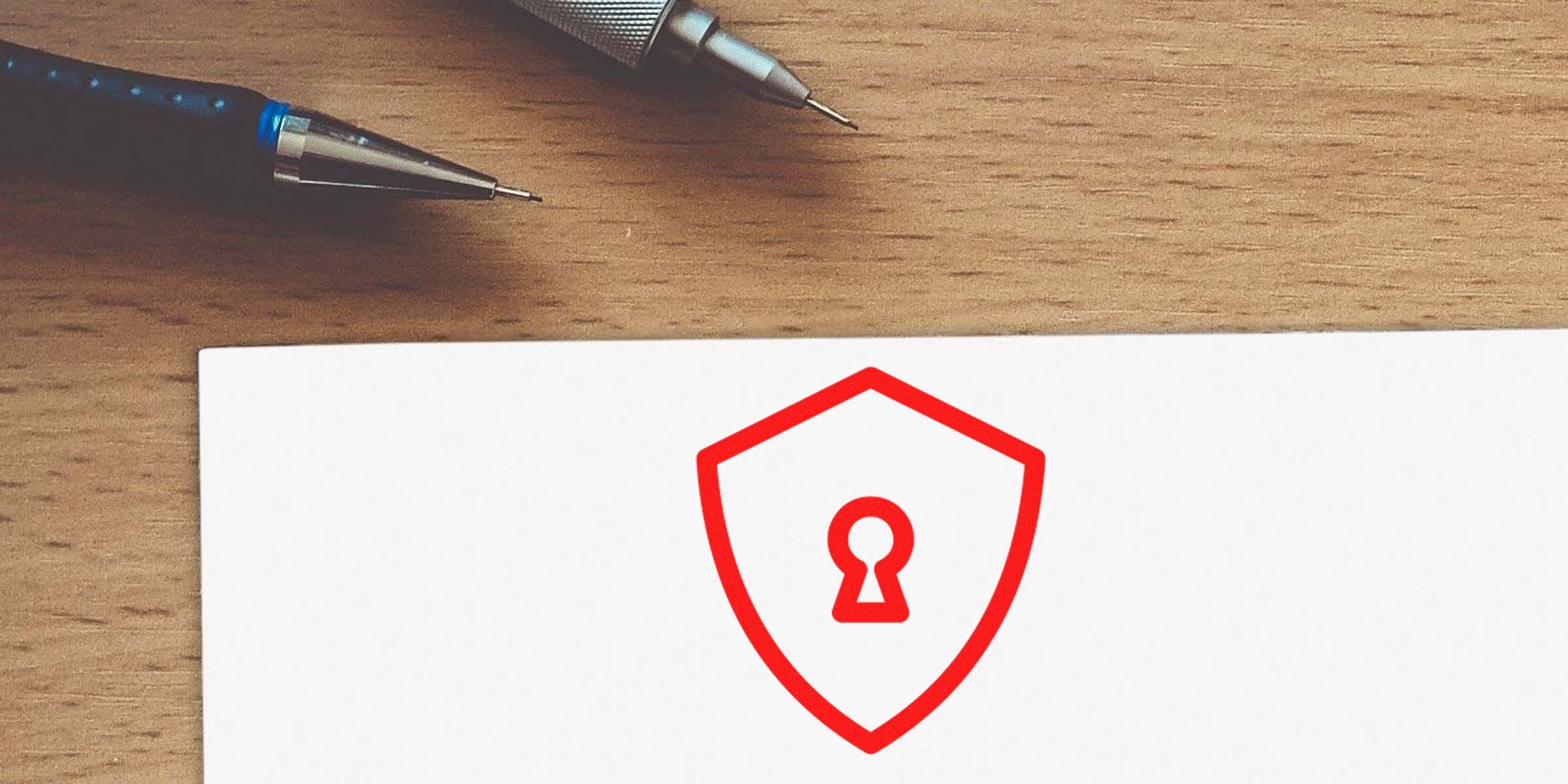 Close-up of a wooden desk with two pens and a white card showing a red shield with a keyhole.