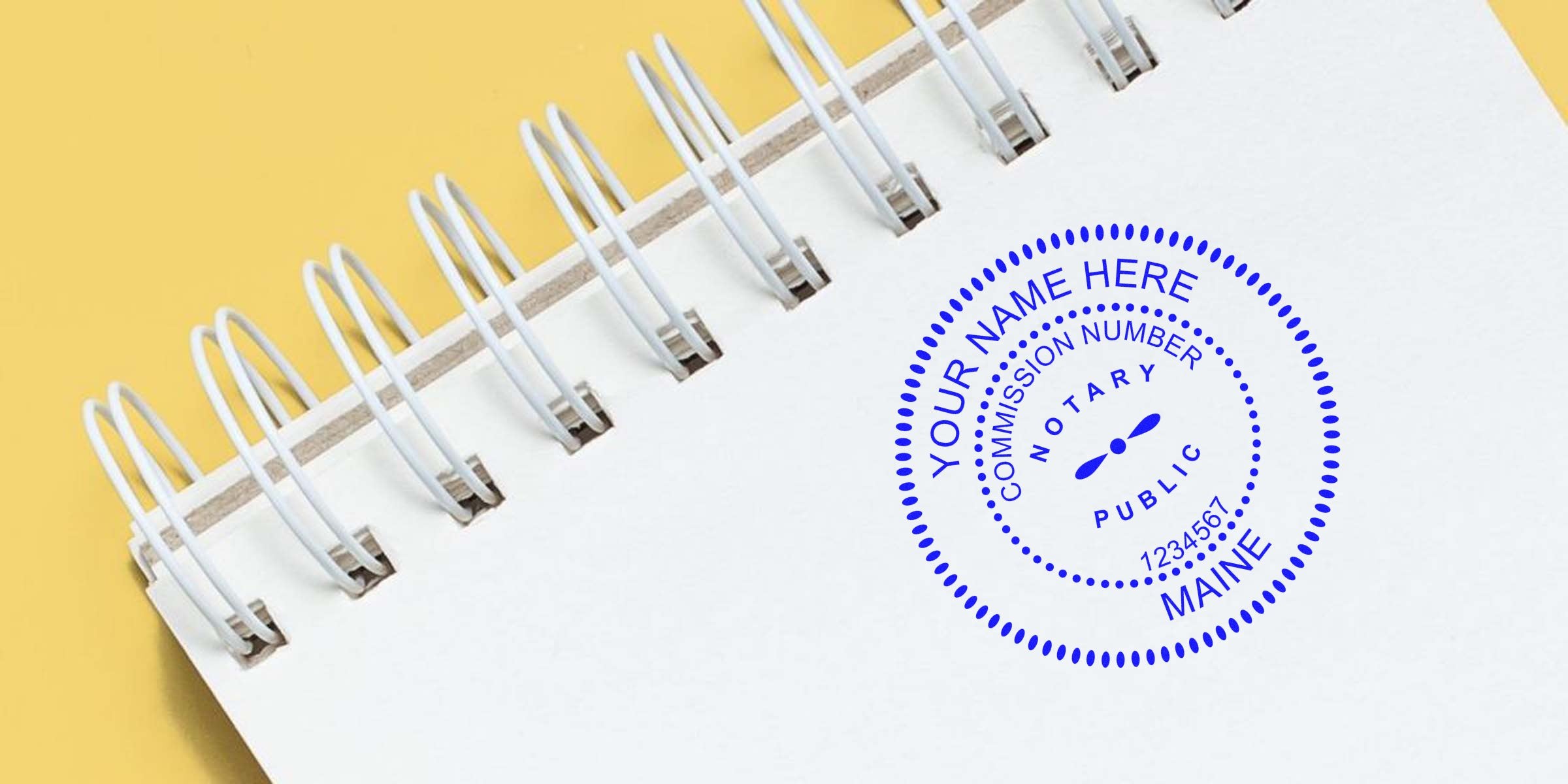 Top-down view of white spiral notebook on yellow background with a blue customizable notary public seal stamp reading "Your Name Here, Maine"