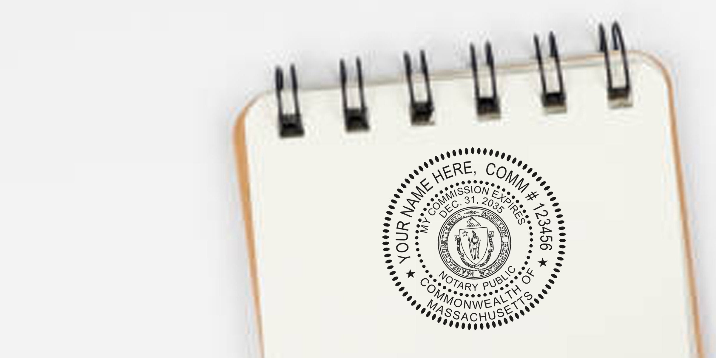 Close-up of black circular Massachusetts notary public seal printed on a cream spiral-bound notebook page, showing concentric dotted border, state emblem, placeholder text "Your Name Here" and commission number.