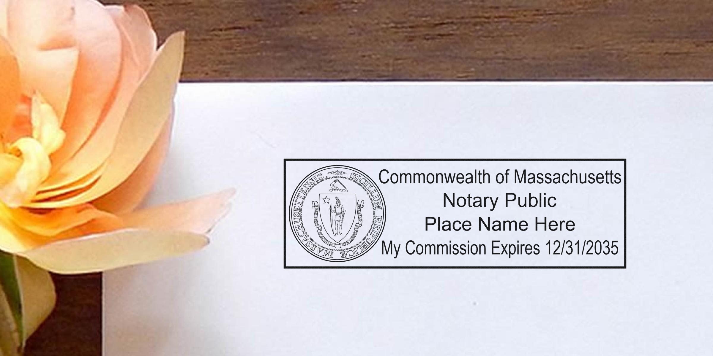 Close-up of a Commonwealth of Massachusetts Notary Public rectangular stamp on white paper reading "Place Name Here" and "My Commission Expires 12/31/2035," with a peach paper flower and wooden tabletop in the background.