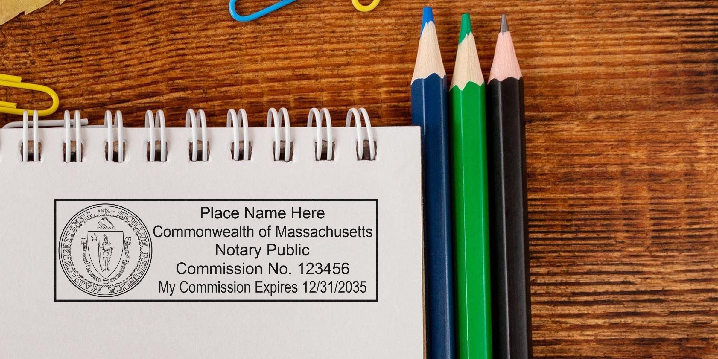 Spiral notebook showing a Massachusetts notary public stamp mockup with commission details, placed next to blue, green and black colored pencils on a wooden desk — business stationery and legal notary concept.